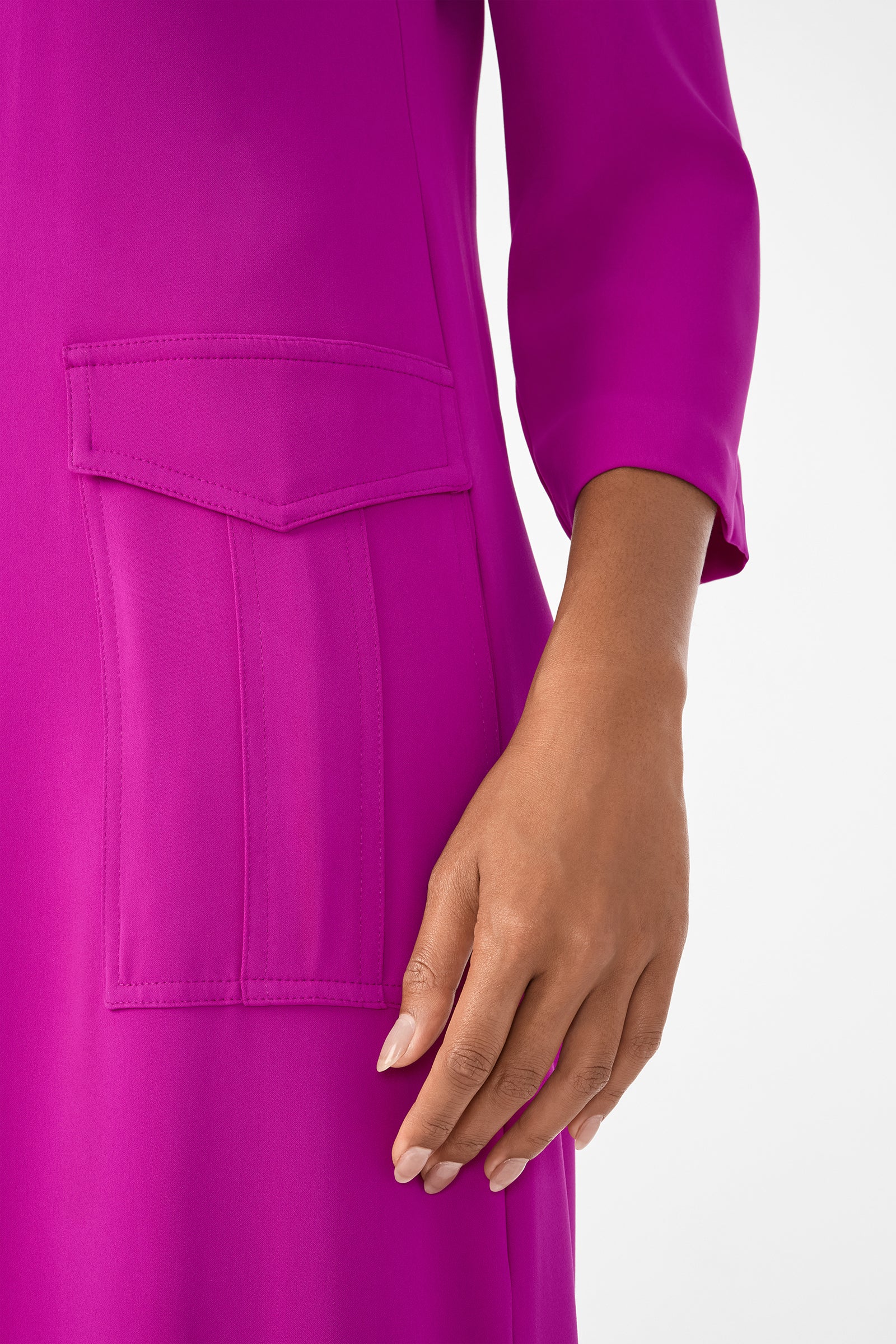 A close-up of a hand near the large flap pocket on the long-sleeved Annecy Dress in bright magenta, set against a plain white background.