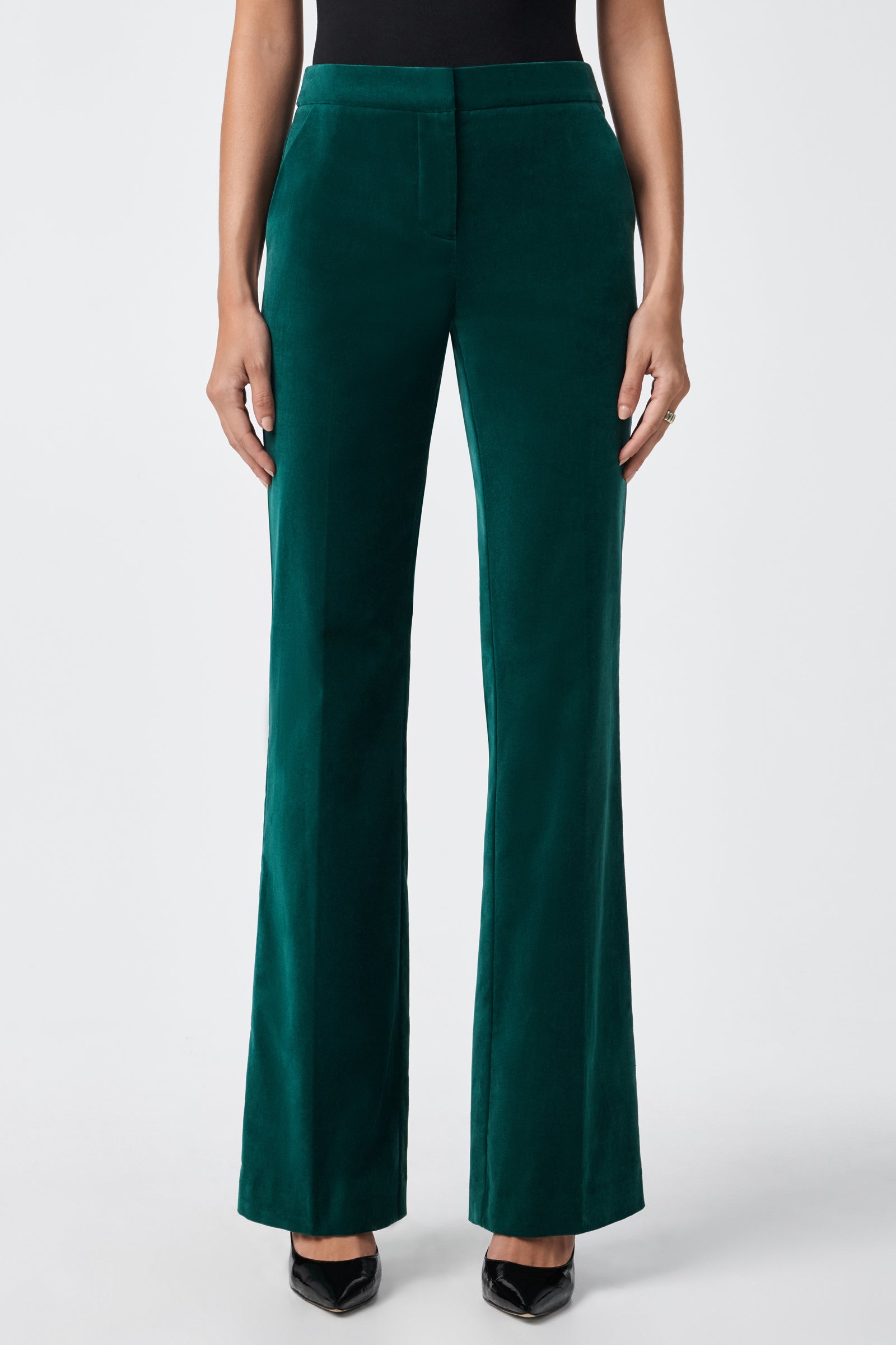 A person wearing the green velvet Westport Pant, styled with black pointed-toe heels, stands against a plain white background.