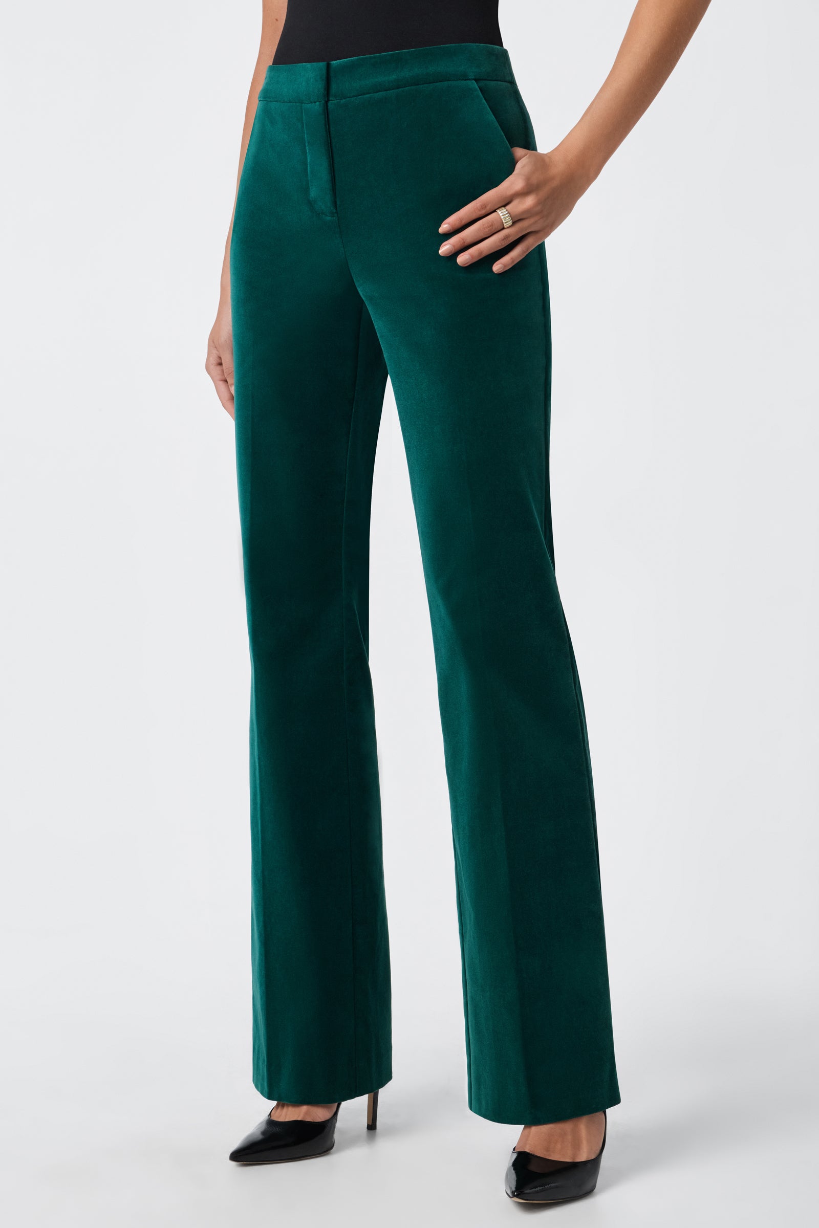 A person wears the Westport Pant, which is high-waisted green velvet, paired with black high-heeled shoes, one hand on their hip against a plain light background.