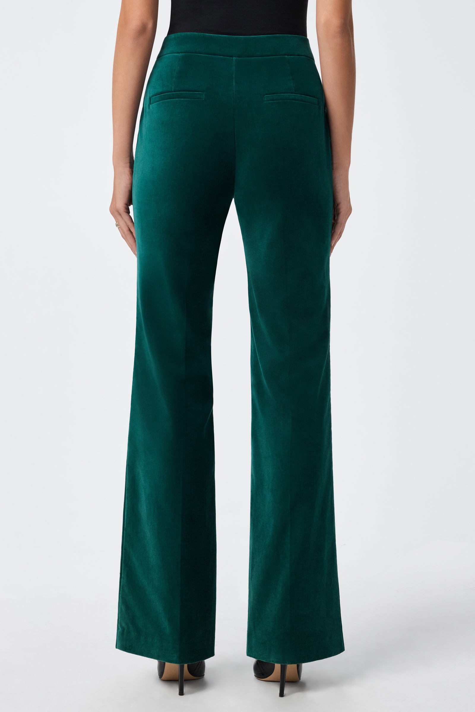 A person wearing the Westport Pant—high-waisted, dark green velvet—paired with black heels, shown from the back against a plain white background.