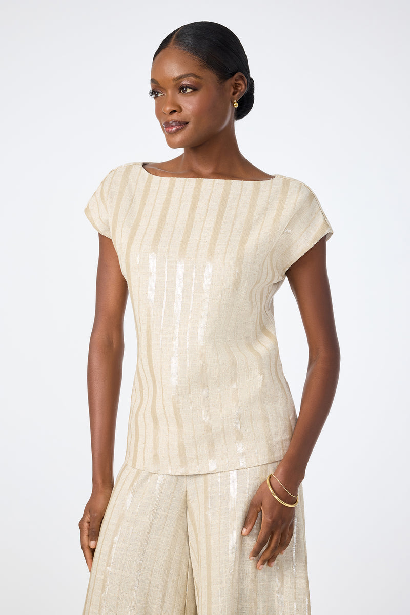 A woman wears the Breene Boatneck Top‚Äö√Ñ√Æa light beige, short-sleeve, striped blouse‚Äö√Ñ√Æpaired with matching wide-leg pants, standing against a plain white background and smiling gently as she looks to the side.