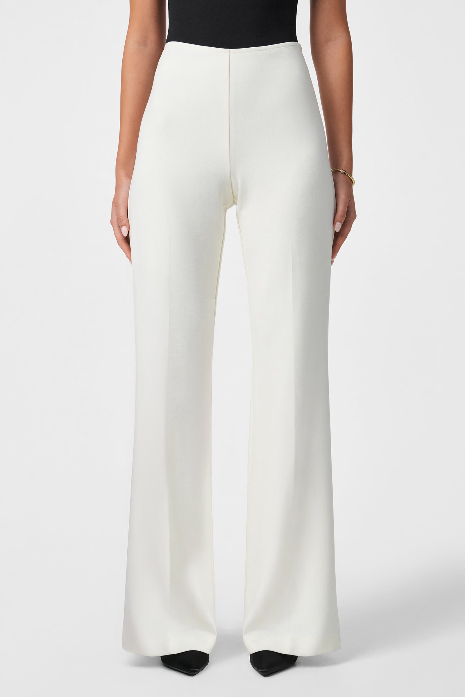 A person models the Chimayo 2 Pant—high-waisted, wide-leg white pants—with a black top and black pointed-toe shoes, standing against a plain white background. Only the lower half of the body is shown.