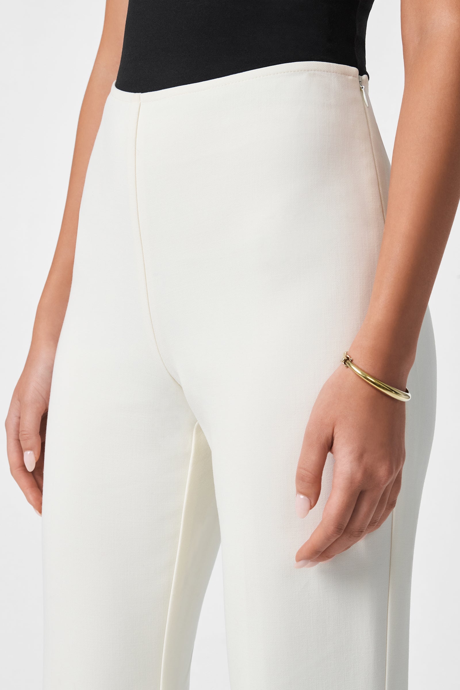 A person wears the Chimayo 2 Pant—high-waisted and white—with a black top and a gold bracelet on their right arm, relaxed by their side. The image is cropped from waist to mid-thigh.