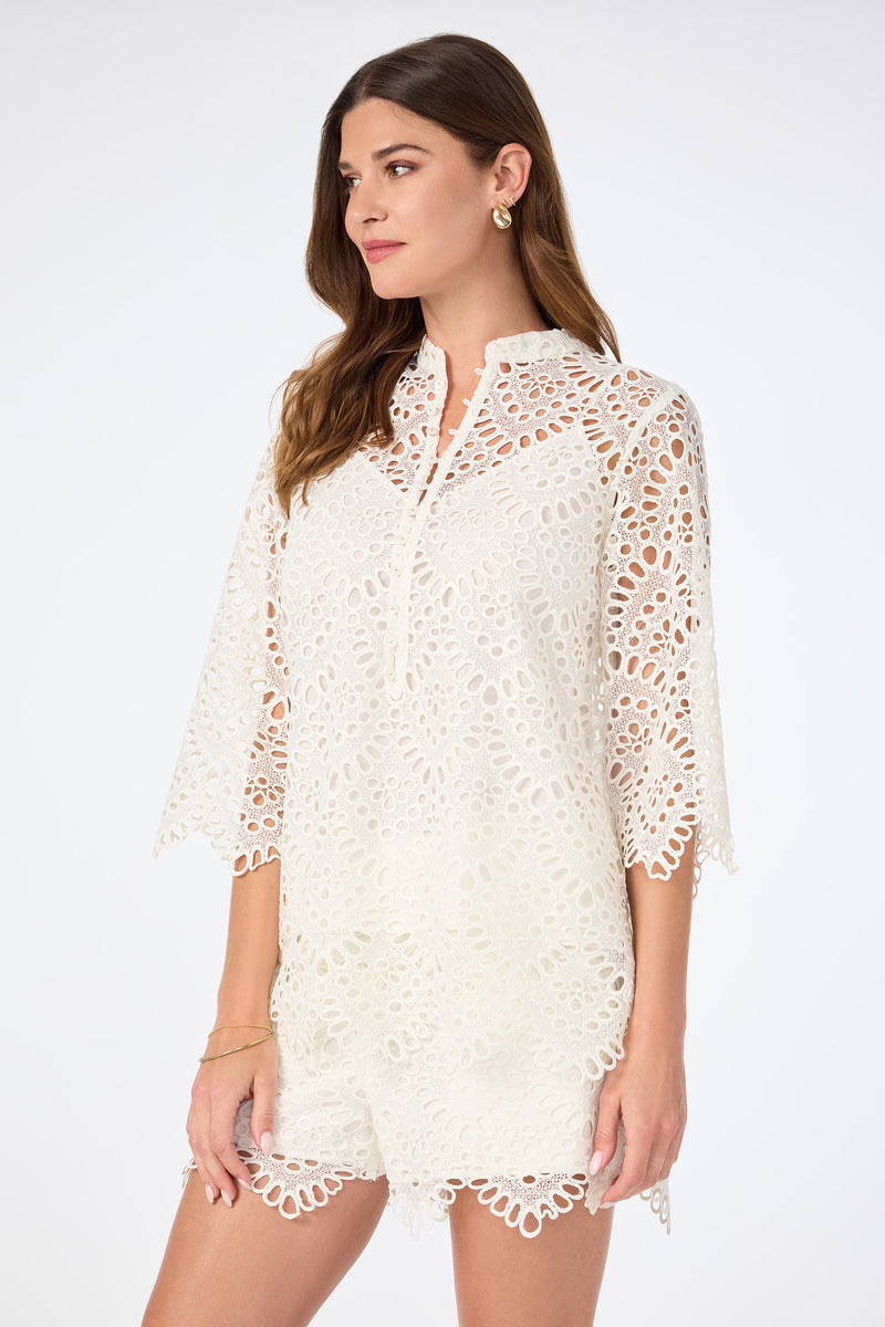 A woman wearing the Martigues Lace Top with gold hoop earrings and a gold bracelet stands against a plain white background.