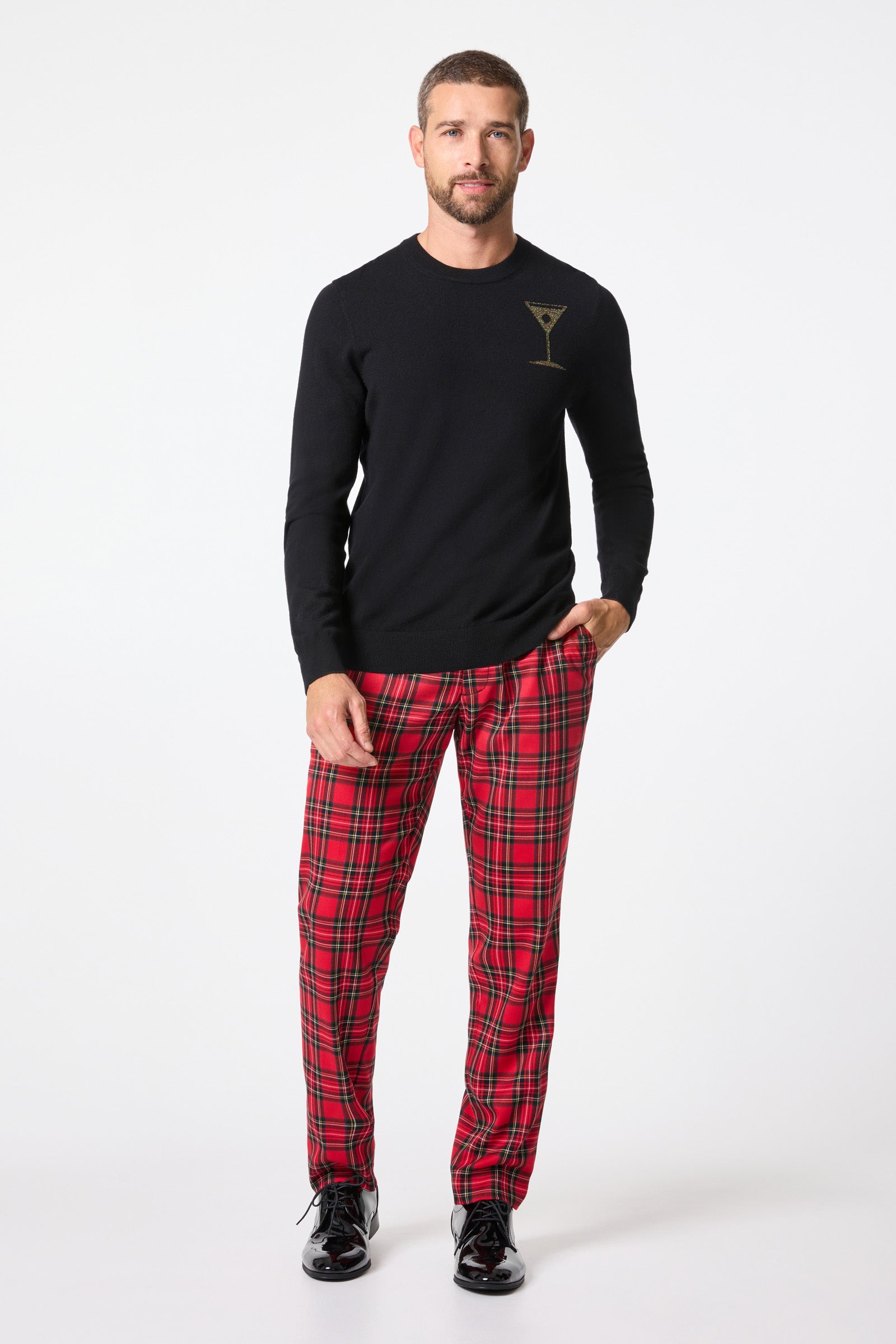 A man wears the Martini Crewneck Sweater featuring a gold martini glass graphic, paired with red plaid pants and shiny black shoes, against a white background.