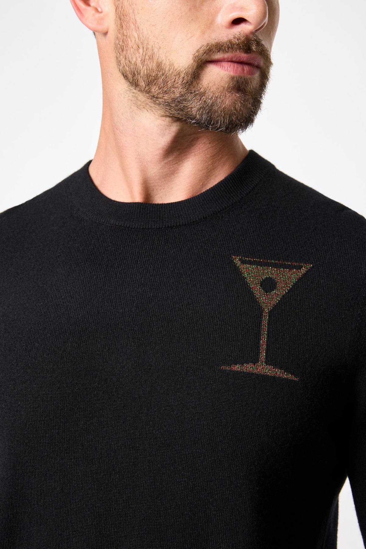 A man models the Martini Crewneck Sweater—black with a small embroidered martini glass on the chest—shown from neck to mid-torso, facing slightly sideways.