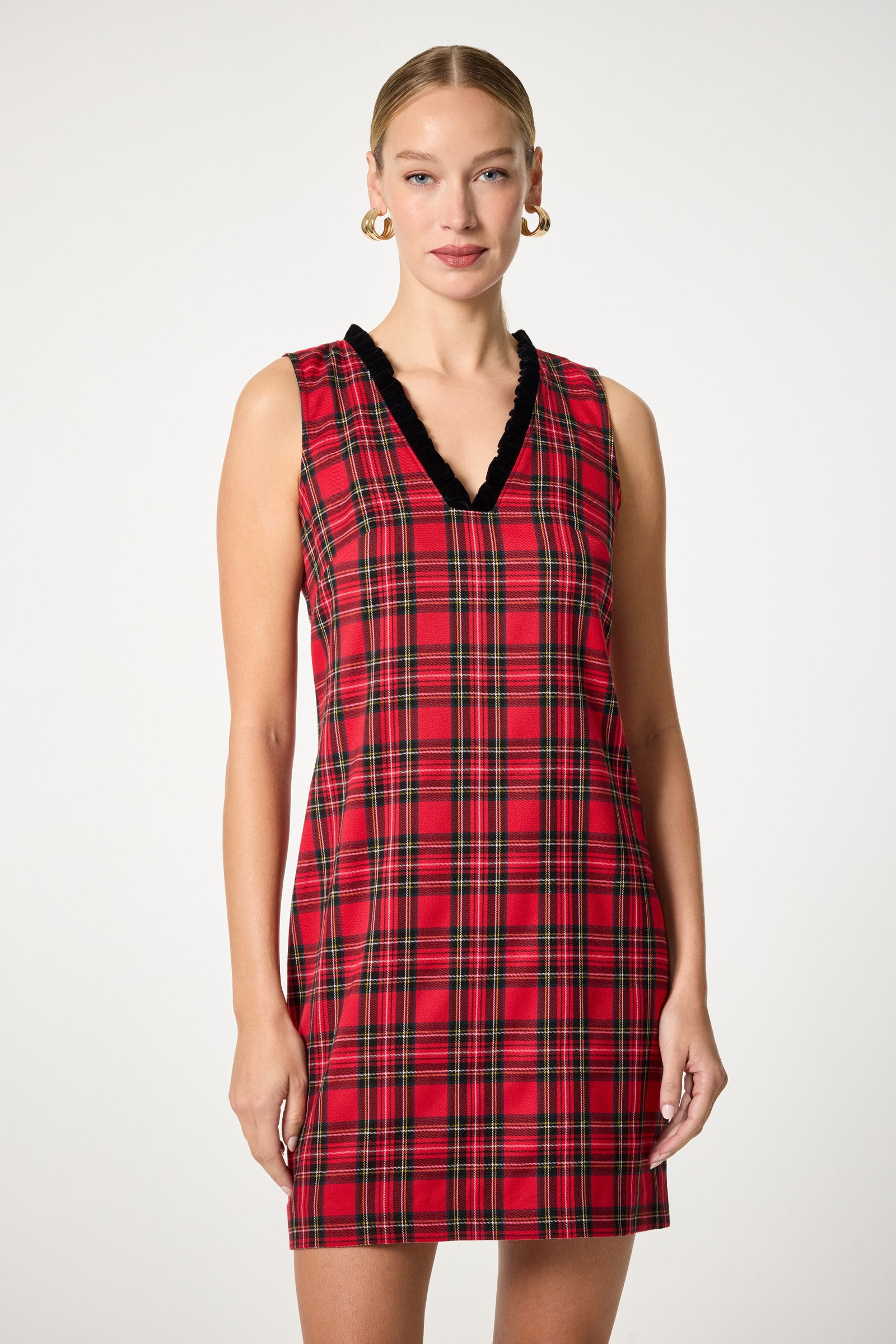 A woman models the Revah Tartan Mini Dress, a sleeveless red plaid dress with black V-neck trim, standing against a plain white background and looking at the camera with a neutral expression.