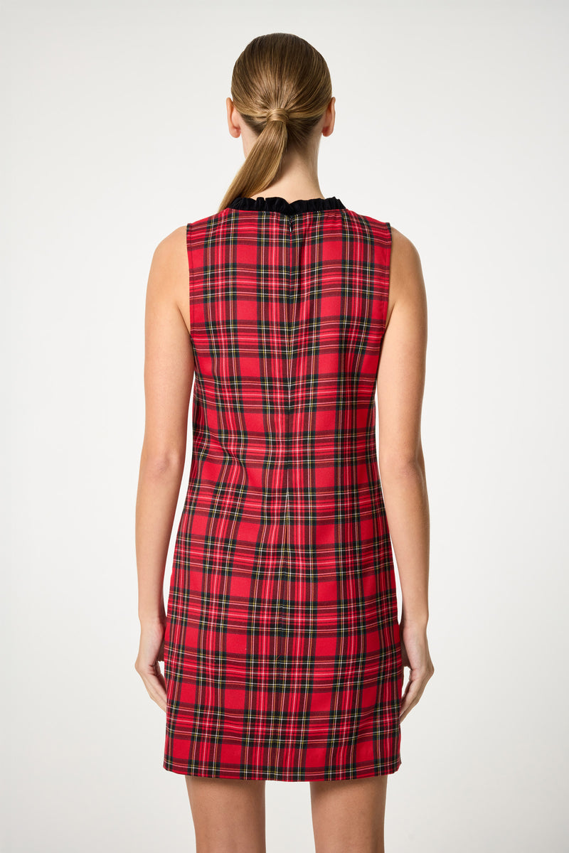 A woman with long, straight hair stands with her back to the camera against a plain, light background, wearing the sleeveless, knee-length Revah Tartan Mini Dress in red plaid.