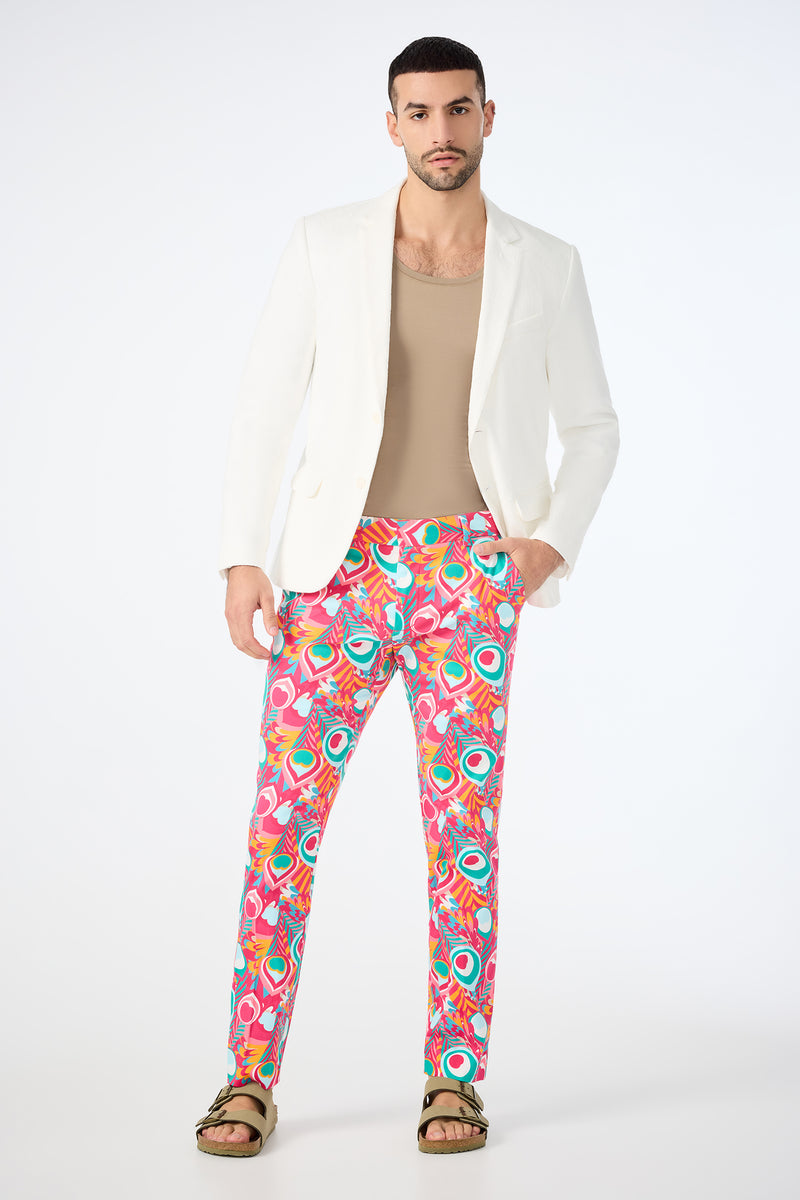 A man stands confidently in the Clyde Slim Trouser - Dramont Herringbone, paired with a white blazer, beige shirt, and brown sandals against a plain white background.