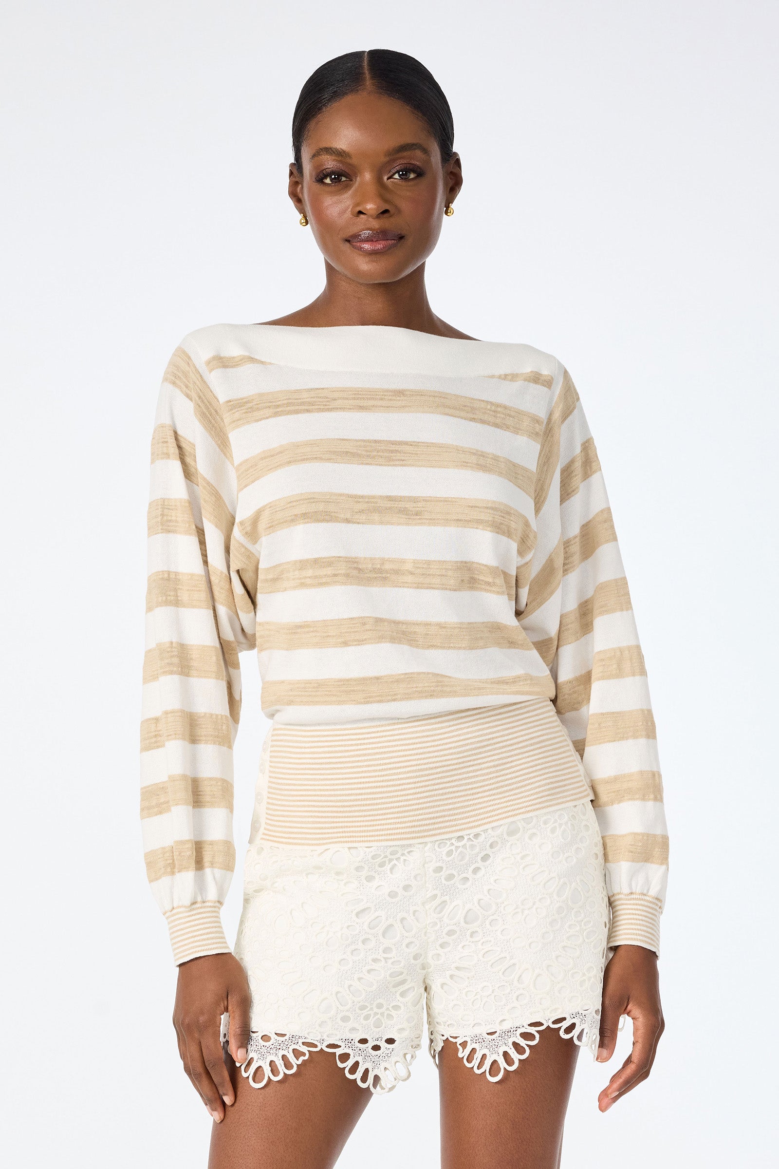 A woman wears the Ramona 2 Boatneck Sweater in Whitewash/Biarritz Beige with cream lace shorts, standing confidently against a plain white background.
