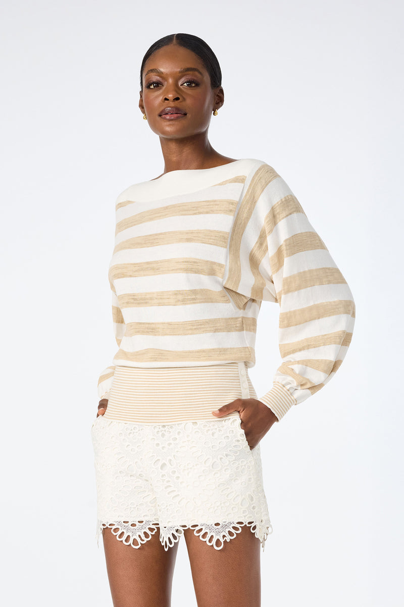 A woman stands against a plain background, wearing the Ramona 2 Boatneck Sweater paired with white lace scalloped shorts. She has her hands in her pockets and looks confidently at the camera.