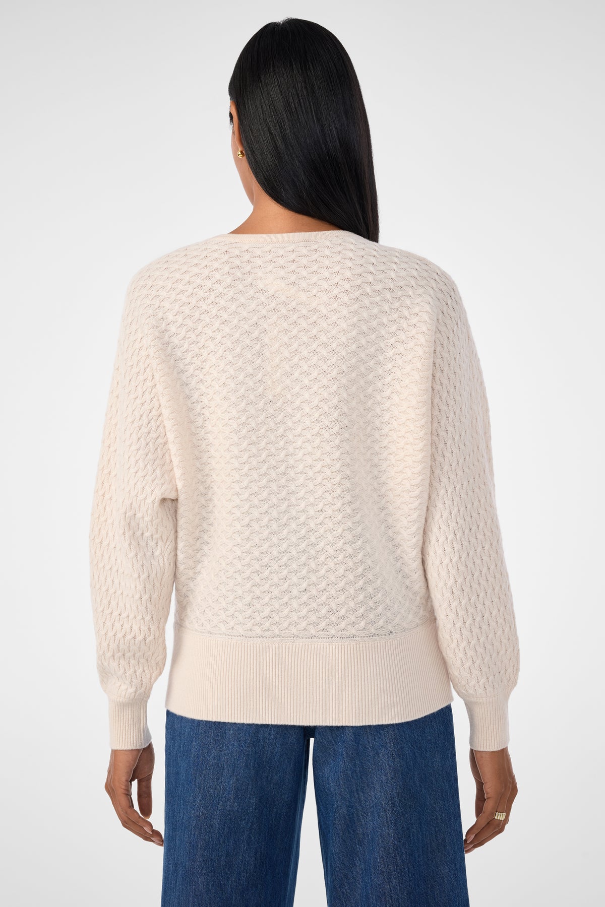 A person with long dark hair, viewed from behind, wears the Lima V-Neck Pullover in cream and blue denim jeans, standing against a plain light background.