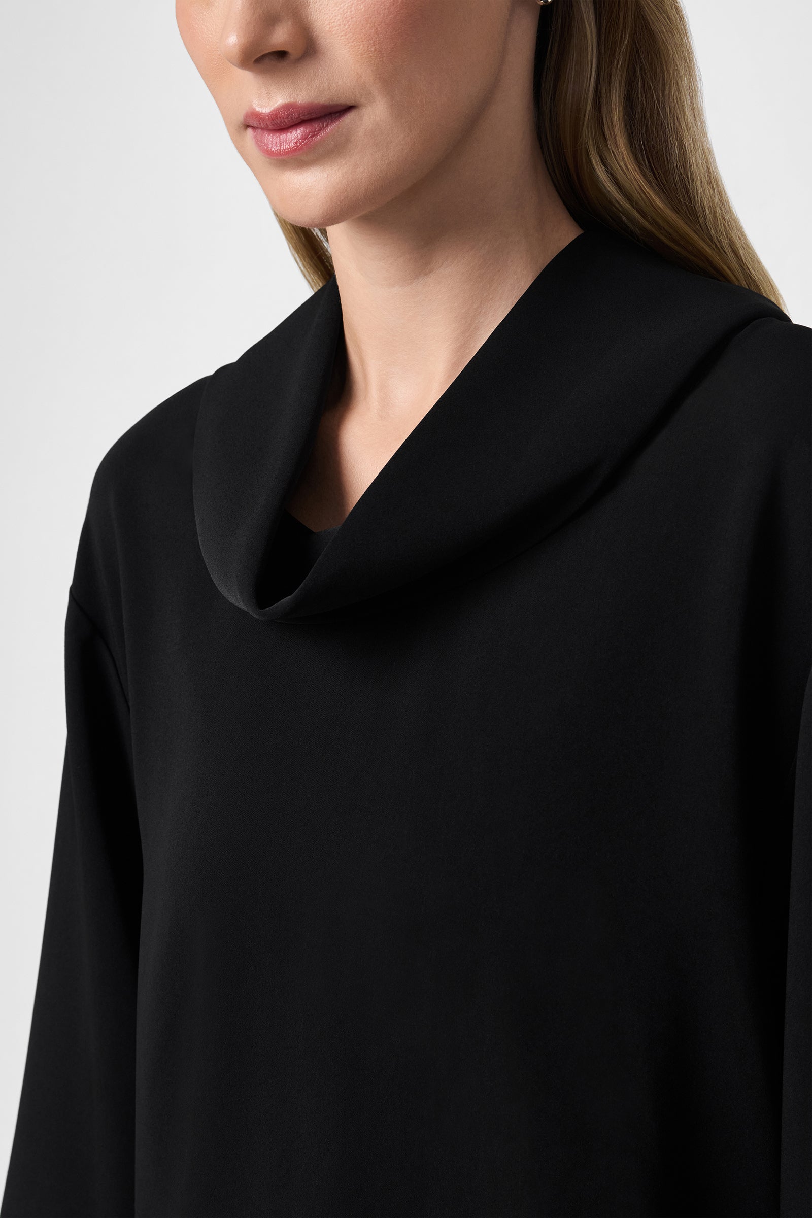 A woman models the Staged Top, a black cowl-neck style. She is shown from the shoulders up, with only the lower half of her face visible against a plain white background.