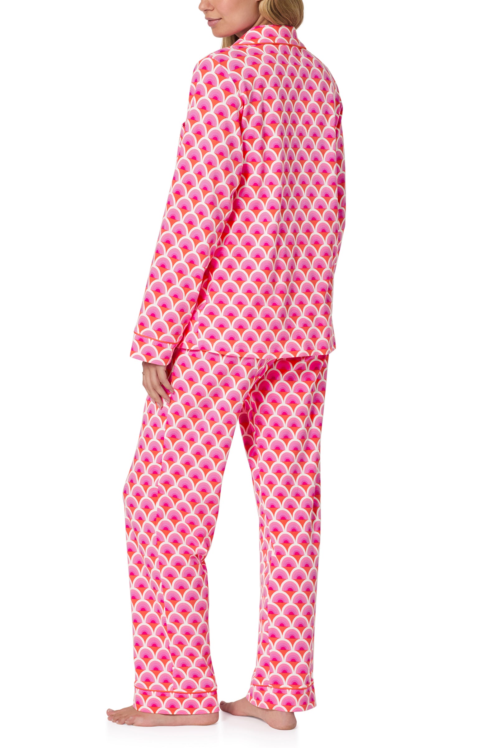 A person stands barefoot, facing away, wearing the Classic PJ Set - Scallop in pink with a white and magenta scallop print. Only their back and side profile are visible.