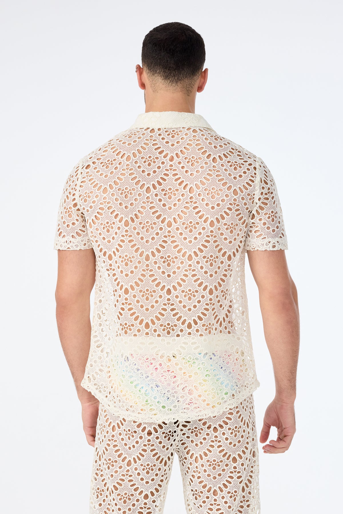 A man stands with his back to the camera in a matching cream Long Beach Short-Sleeve Shirt and pants set, both featuring intricate crochet lace openwork patterns, against a plain white background.