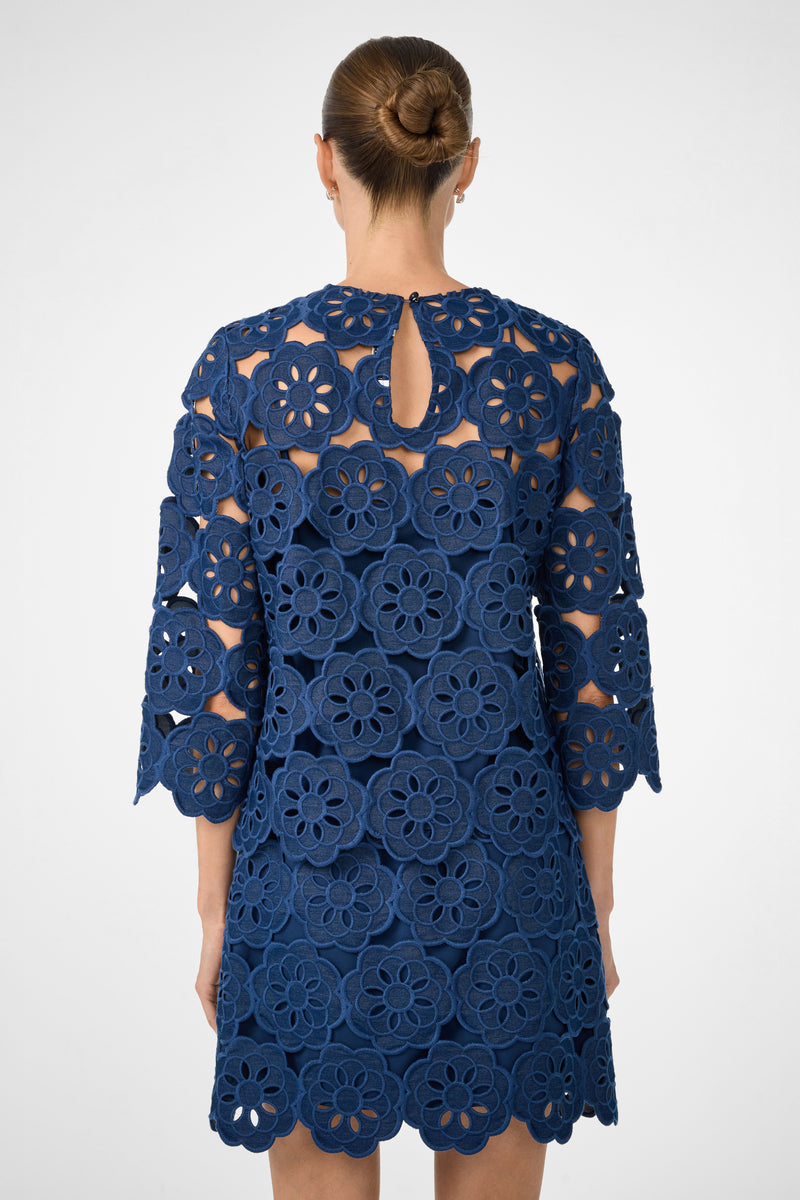 A woman with her hair in a bun is seen from the back wearing the Kabosu Top - Kusho Embroidery, a navy blue piece featuring large floral cutout lace patterns and three-quarter sleeves.