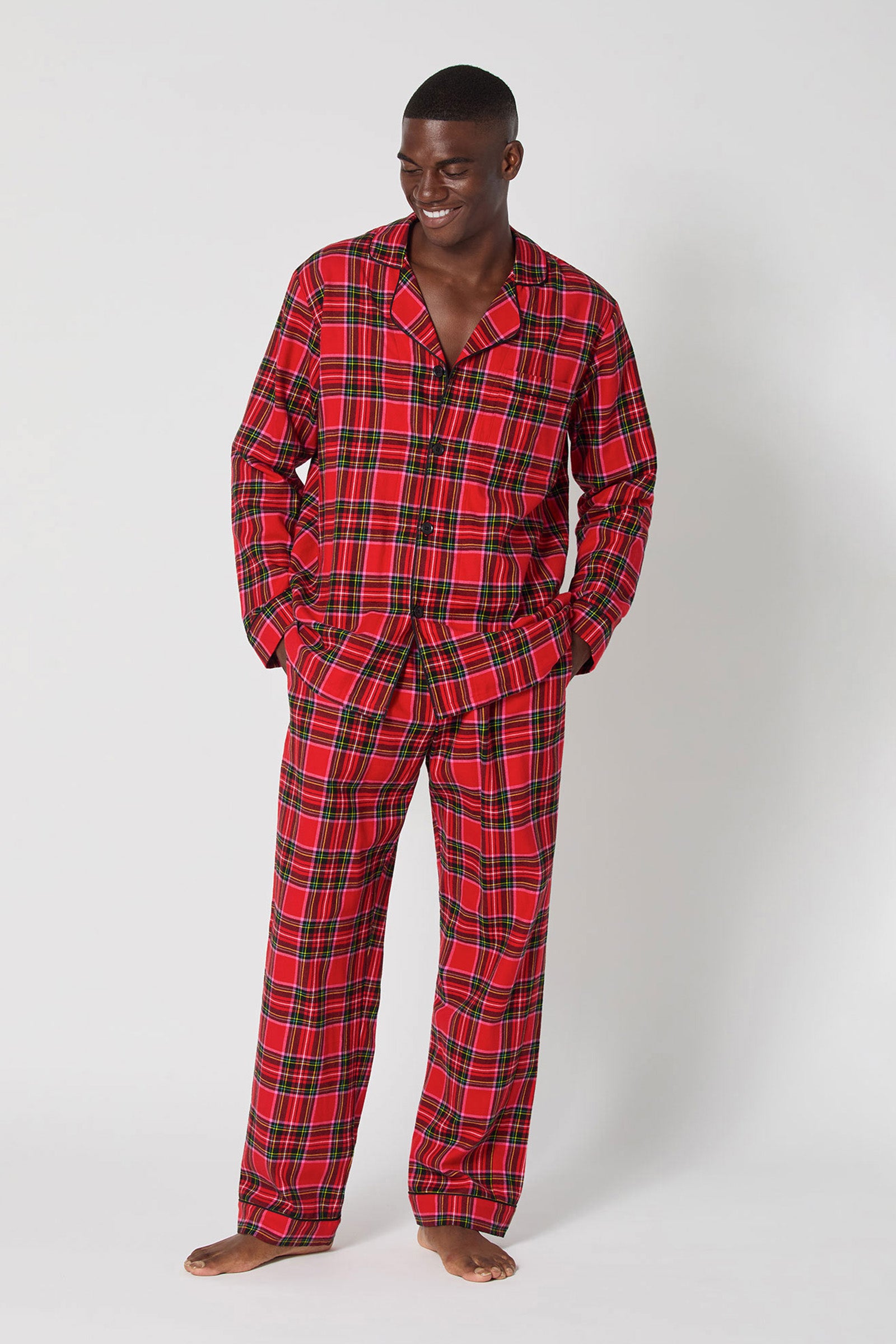 A smiling man stands barefoot in Christmas Plaid Men Classic Pj, hands in his pockets, against a plain light background.
