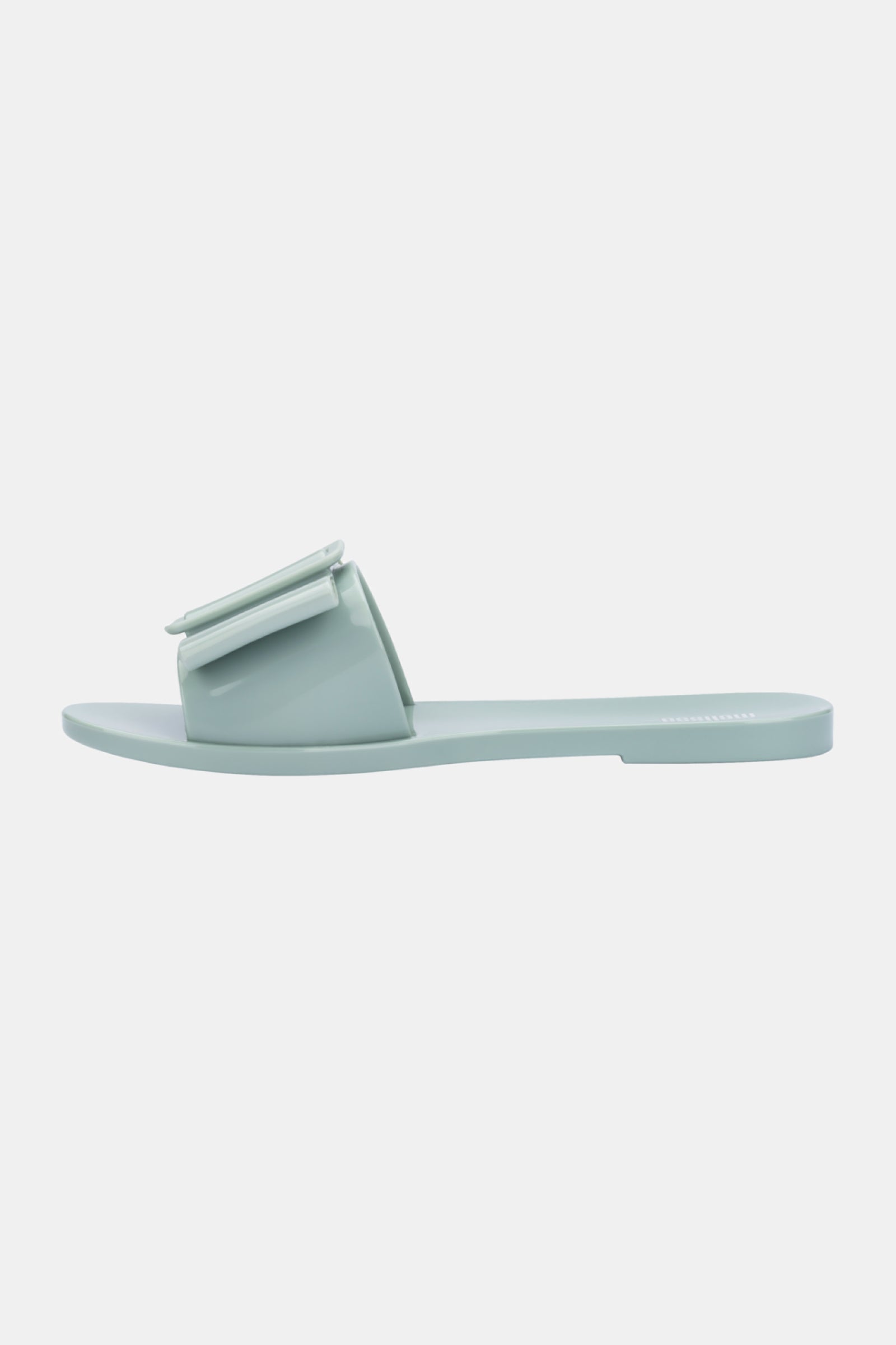The Melissa Babe Sandal is a light blue slide with a flat sole and wide front strap, featuring a decorative rectangular accent. This sandal offers a minimalist, modern design.
