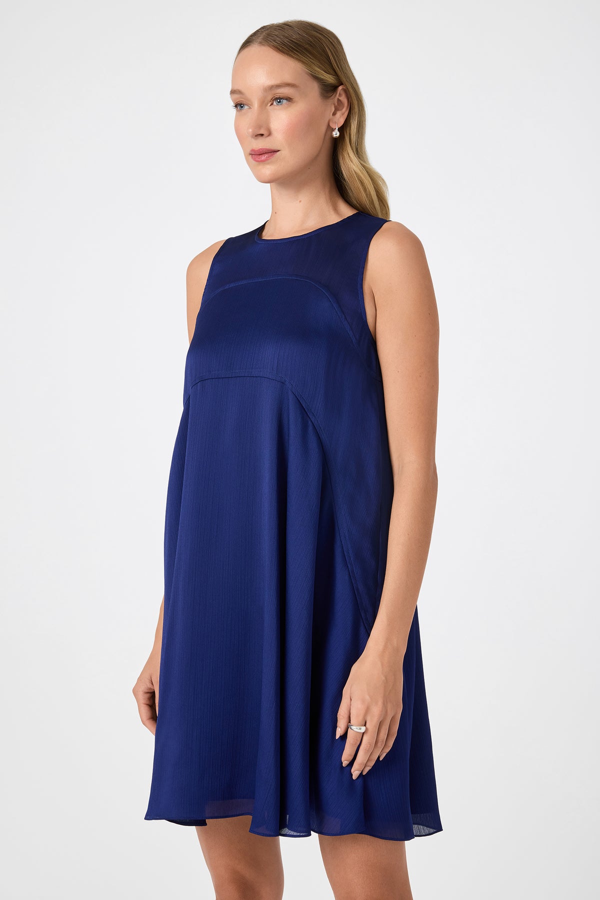 A woman with long blonde hair wears the Mauvie Sleeveless Mini Dress in dark blue, standing against a plain white background and looking slightly to the side with a neutral expression.