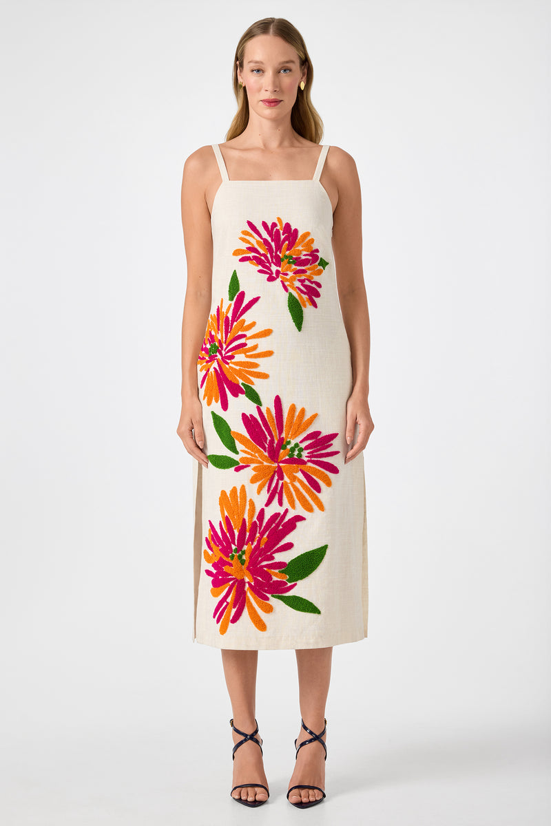 A woman stands facing forward in the Yona Embroidered Flowers Midi Dress‚Äîan ankle-length, sleeveless cream dress with bold pink, orange, and red floral prints. She wears strappy black sandals and has straight hair, set against a plain white background.