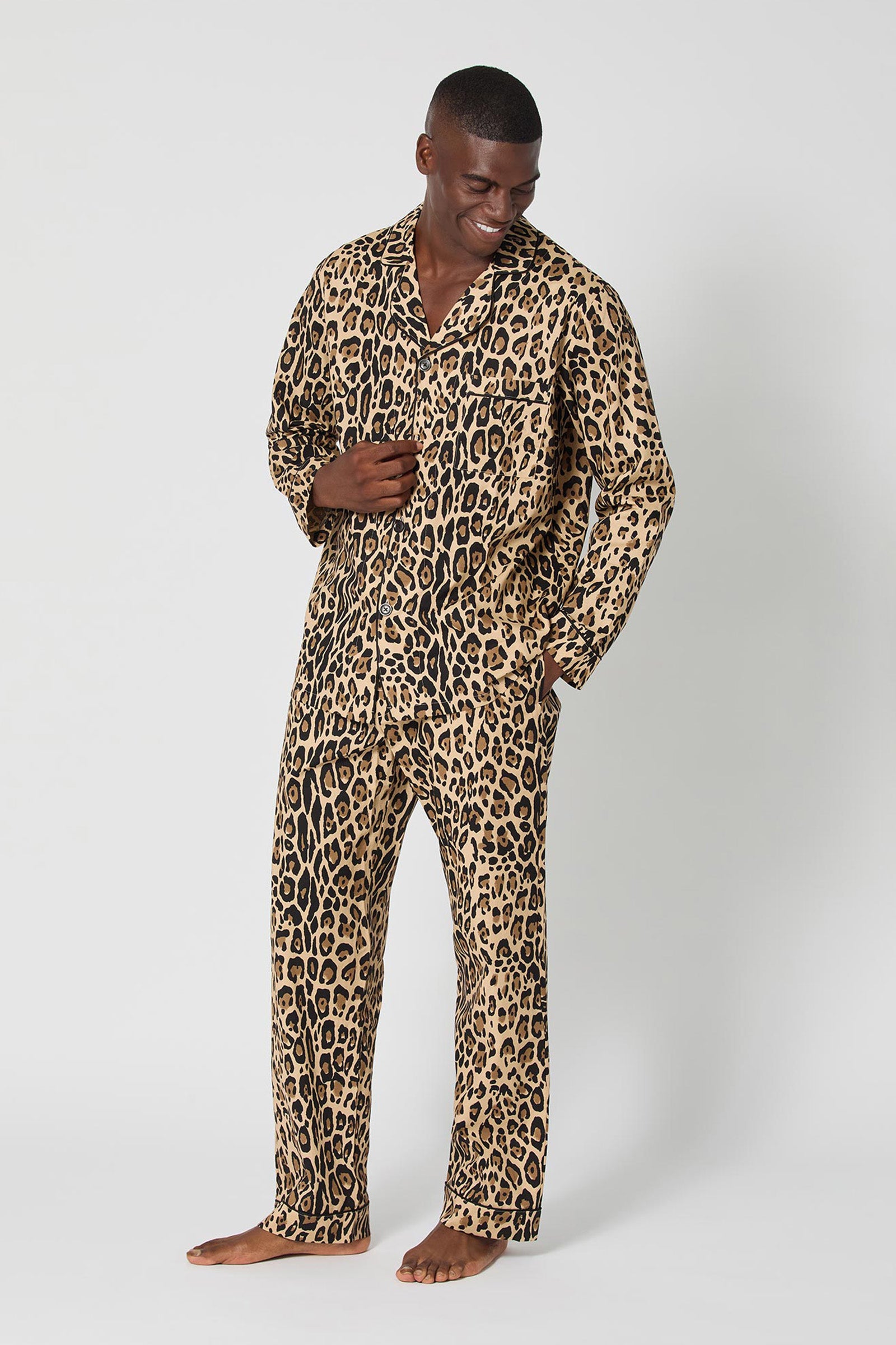 A man stands barefoot and smiling, modeling the Leopard Stripe Mens Classic Pj—a matching set with a bold leopard print—against a plain light gray background.