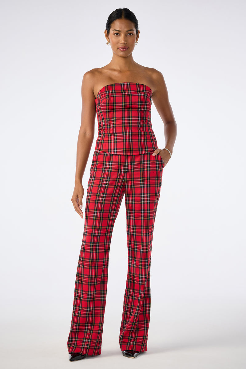 A woman stands against a plain background wearing the Arden Top, a strapless, fitted red plaid top, paired with matching high-waisted, wide-leg plaid trousers.