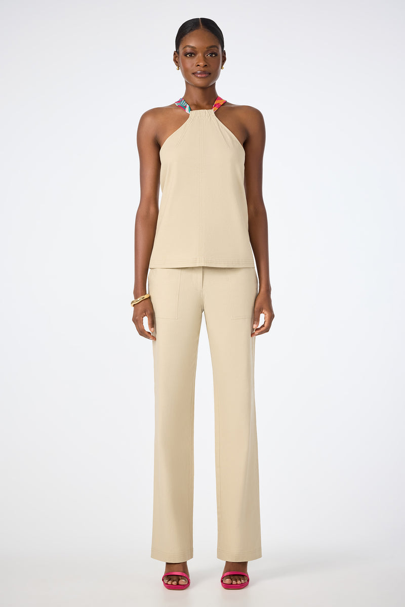 A woman faces forward wearing the beige Chatone Scarf Tie Halter Top with matching wide-leg pants, pink open-toe heels, hoop earrings, and a gold bracelet against a plain white background.