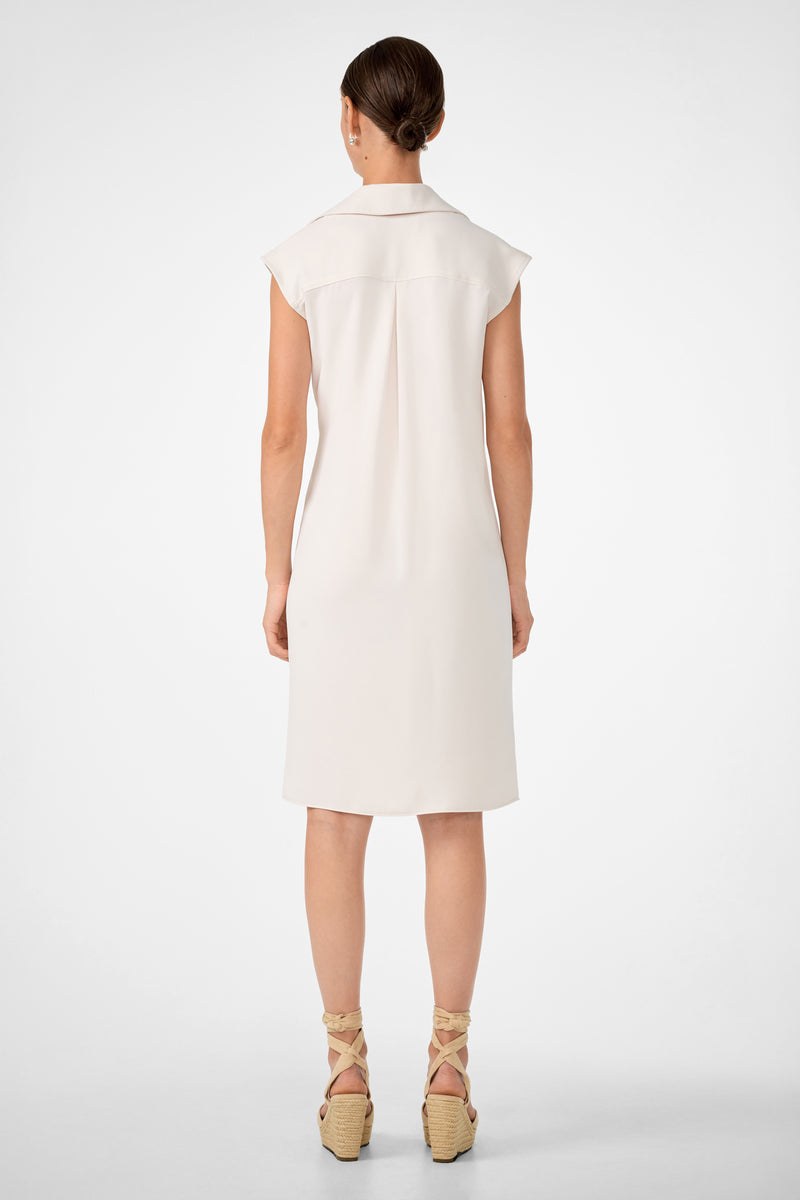 A woman with brown hair in a low bun stands with her back to the camera, wearing the Meron Short-Sleeve Tie-Front Dress and beige wedge sandals with ankle ties, against a plain white background.