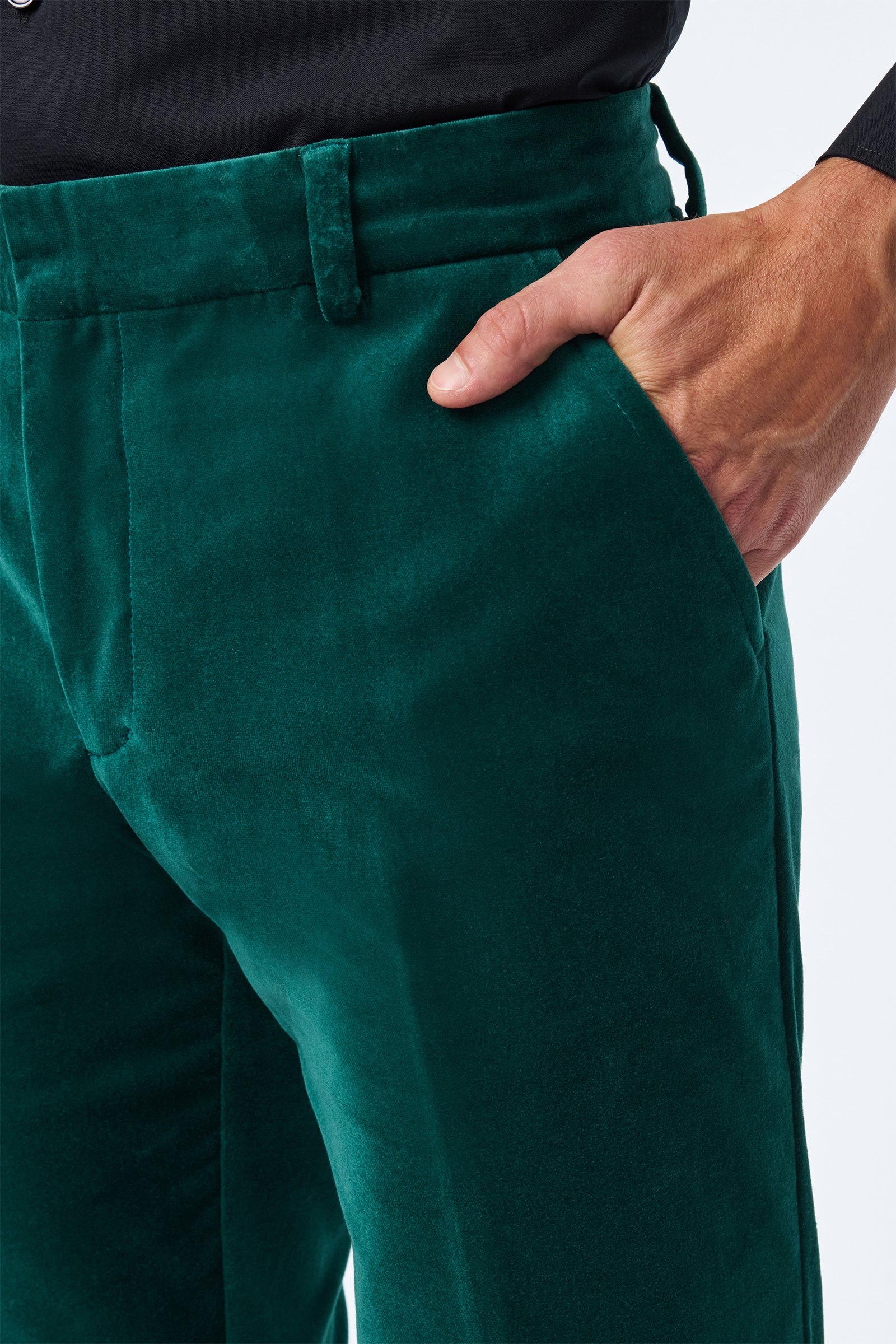 Someone wearing the Clyde Slim Velvet Trouser in dark green with a black shirt has their right hand in the trouser pocket. Only their lower torso and upper legs are visible.
