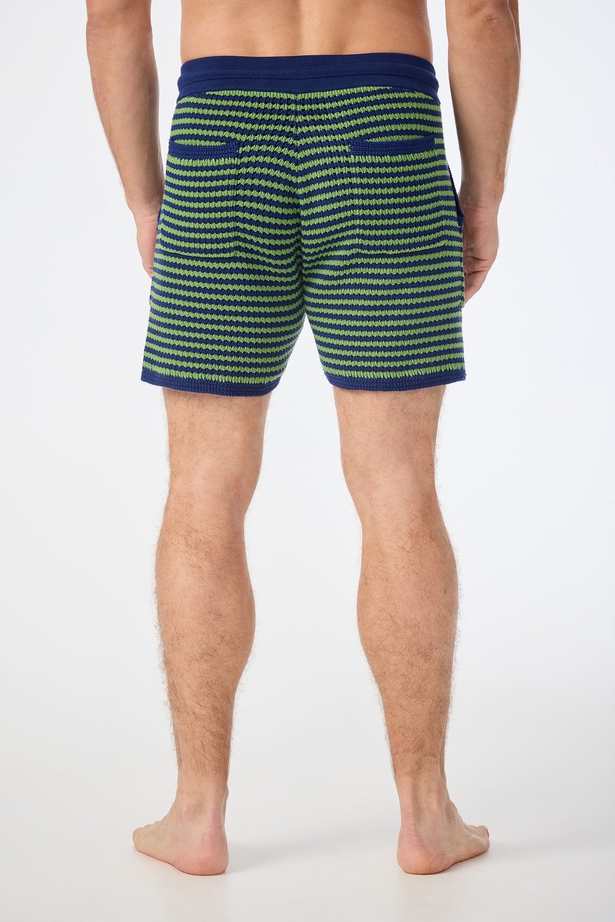 A man stands barefoot on a white background, shown from the back, wearing August Knit Shorts‚Äîpatterned in green, blue, and white with a blue waistband and pocket trim‚Äîcut to mid-thigh length.