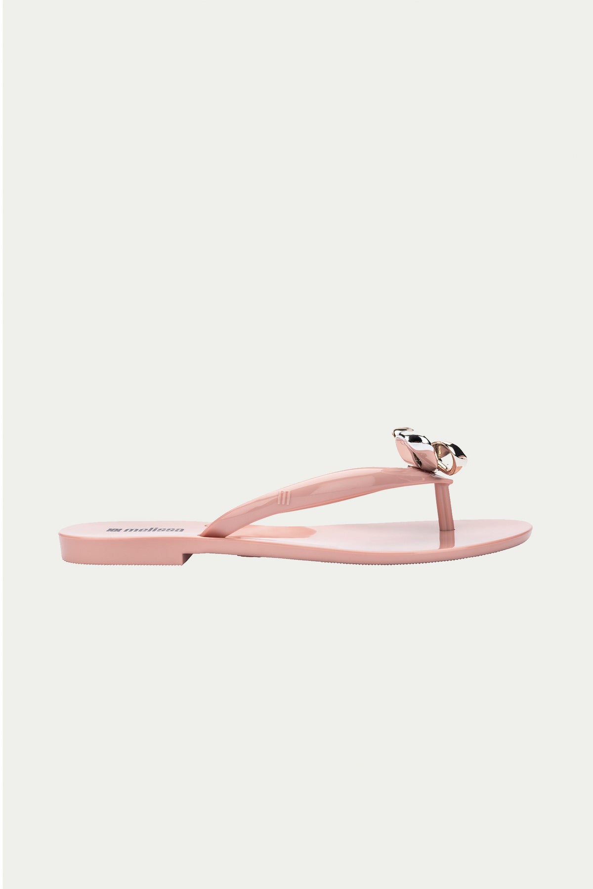 The Melissa Harmonic Eclipse Bow Sandal in pink features a light pink thong strap design with a metallic bow, shown in profile on a plain white background.