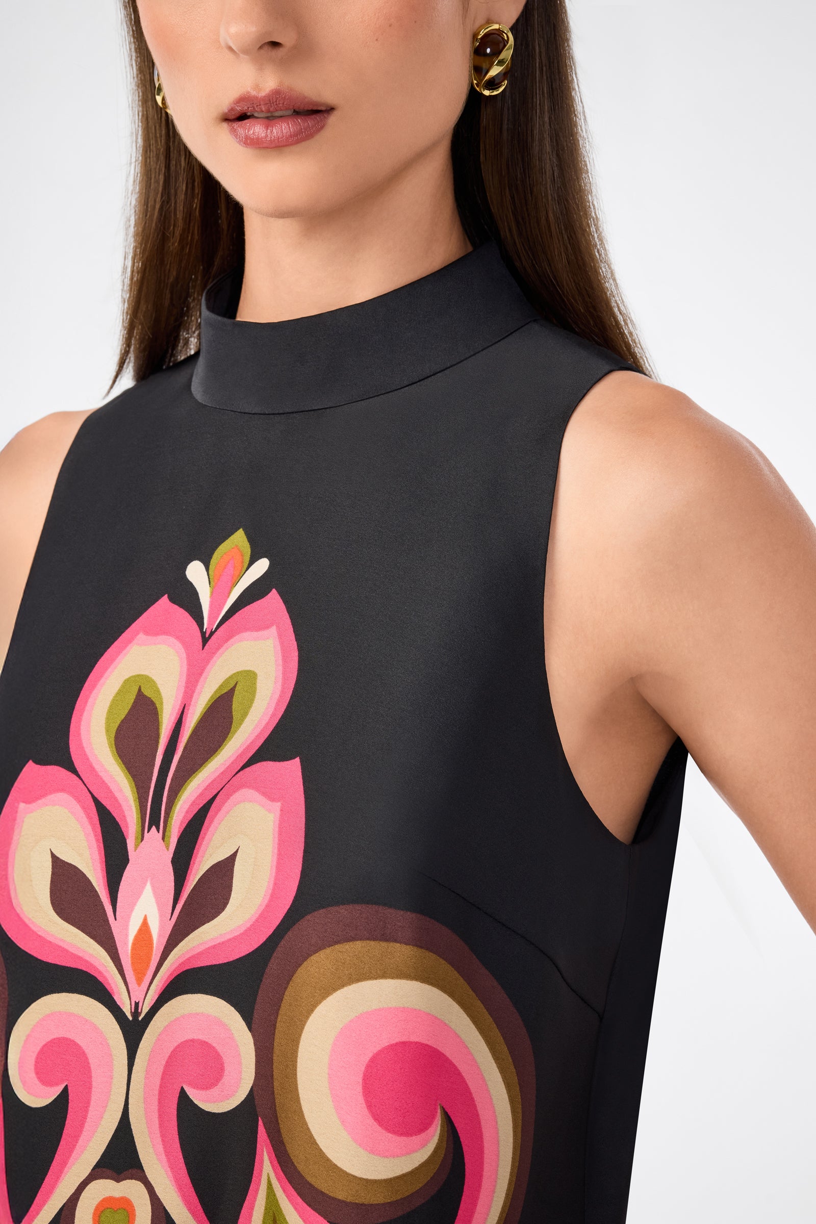 A woman wears the Loveage Sleeveless Maxi Dress, featuring a high neckline and a bold pink and brown abstract floral pattern. She has straight brown hair, gold hoop earrings, and only her upper body is visible.