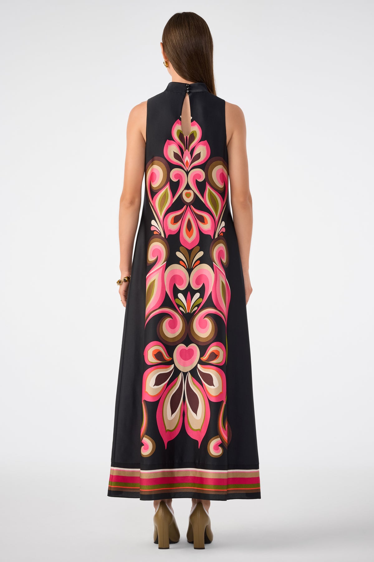 A woman with straight brown hair faces away from the camera, wearing the Loveage Sleeveless Maxi Dress—a black maxi dress featuring a striking pink, red, and cream floral pattern down the back—paired with high-heeled shoes.