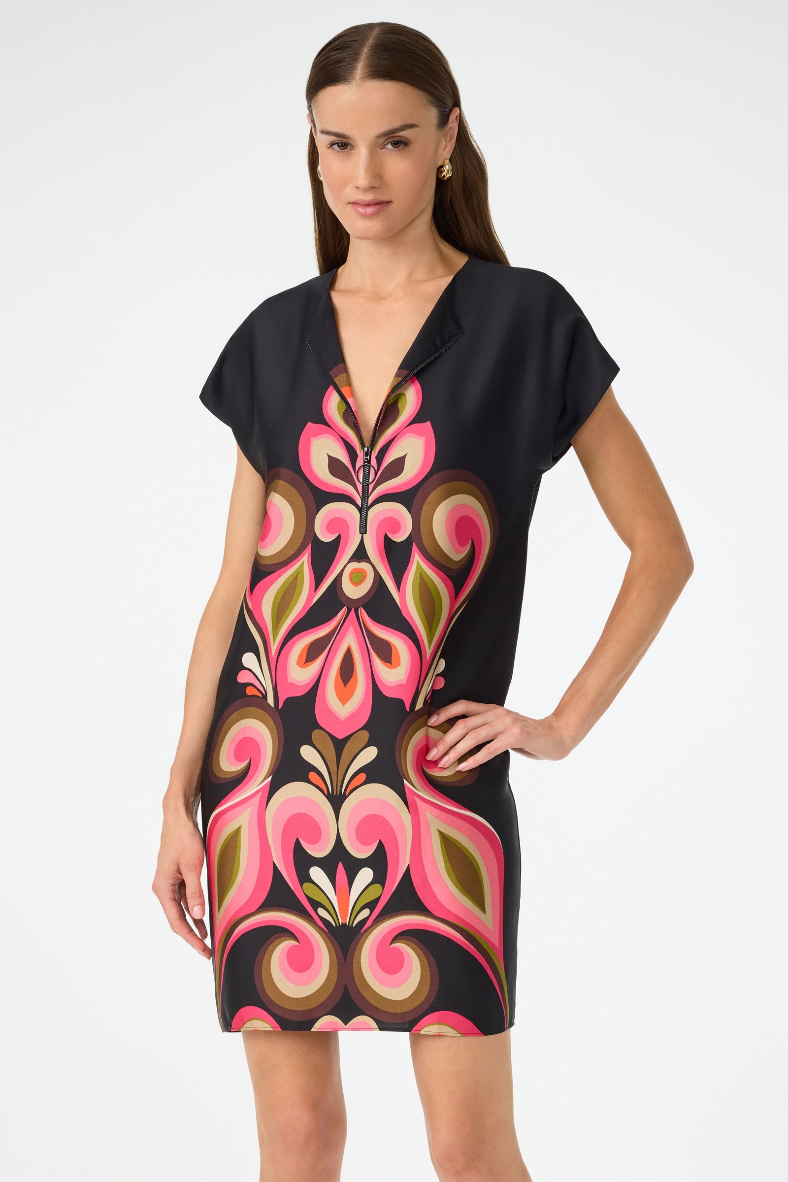 A woman wears the Hasil 3 Short-Sleeve Shift Dress by Sanctuary, featuring a deep V-neck and bold pink and green abstract patterns on black, standing against a plain white background.