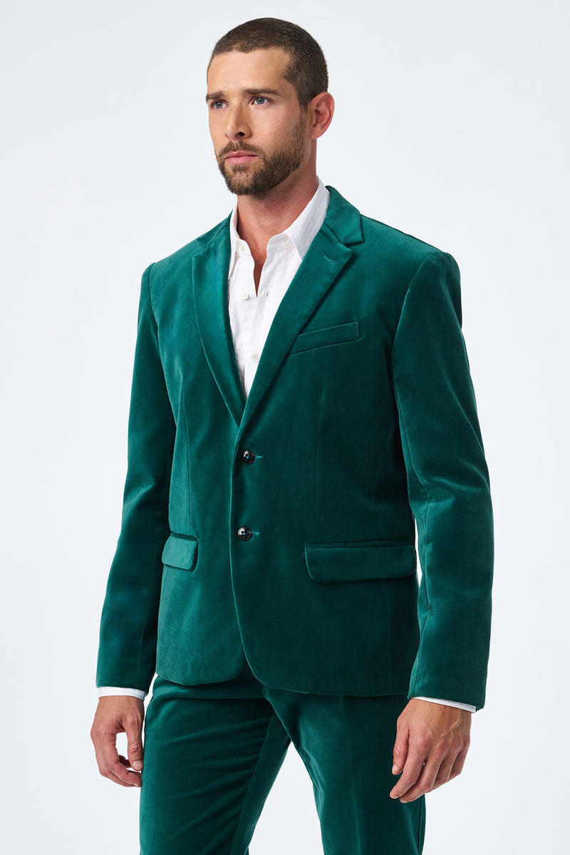 A man with short brown hair and a beard wears the Thurston Velvet Blazer in green with matching pants over a white dress shirt, standing against a plain light background.