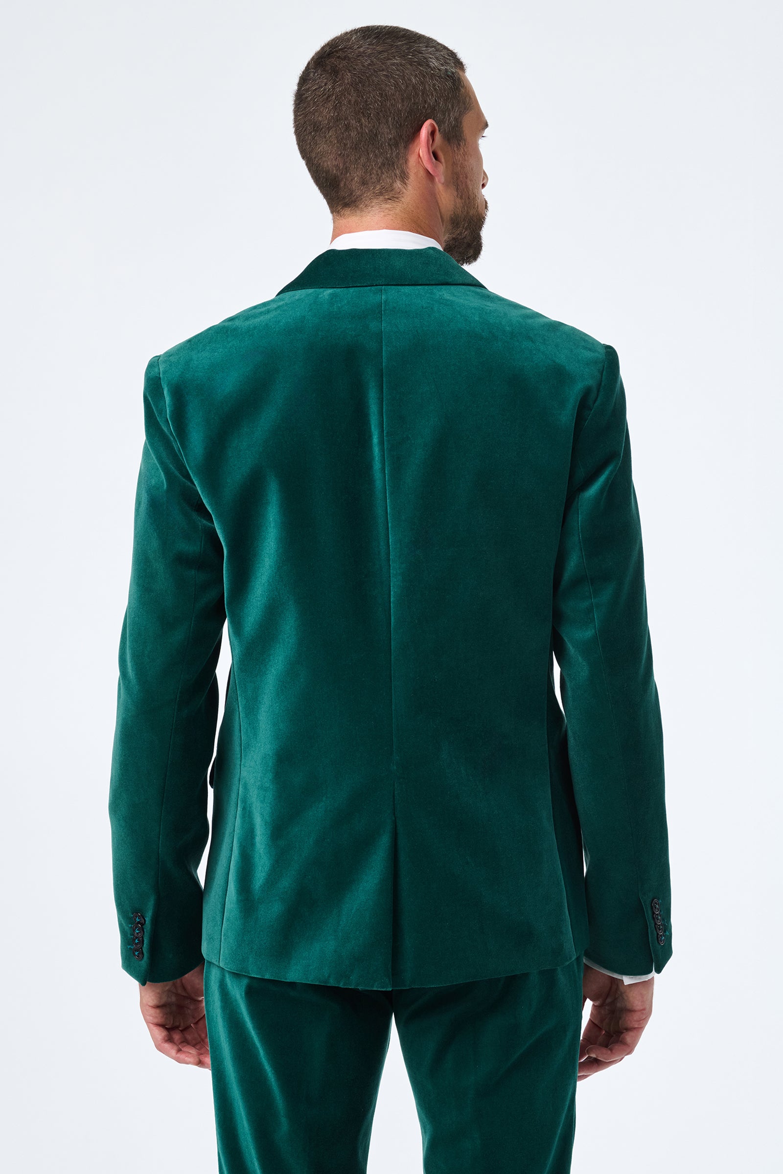 A man with short hair faces away from the camera, modeling the back of the Thurston Velvet Blazer and matching pants in green against a plain white background.