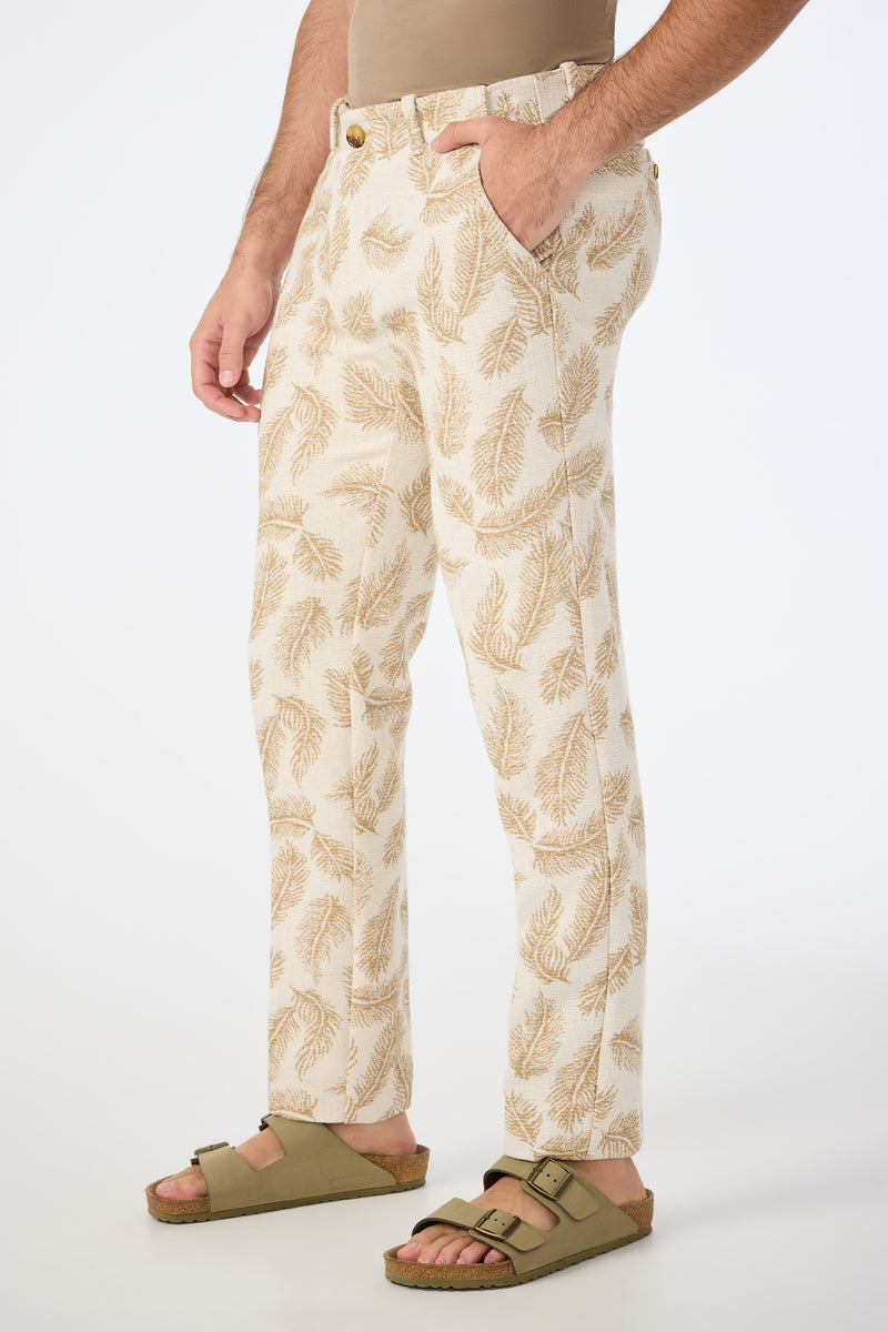Wearing the Alex Slim Trouser in Desert Fronds Jacquard, a person stands with one hand in their pocket against a plain white background.