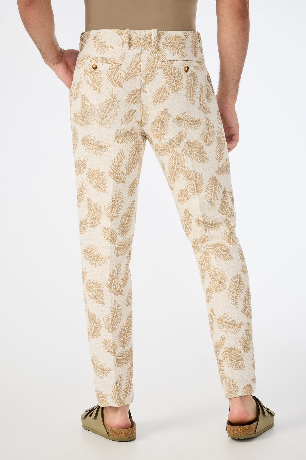 A person stands facing away, wearing the Alex Slim Trouser in Desert Fronds Jacquard with a tan shirt tucked in and tan suede moccasins, set against a plain white background.