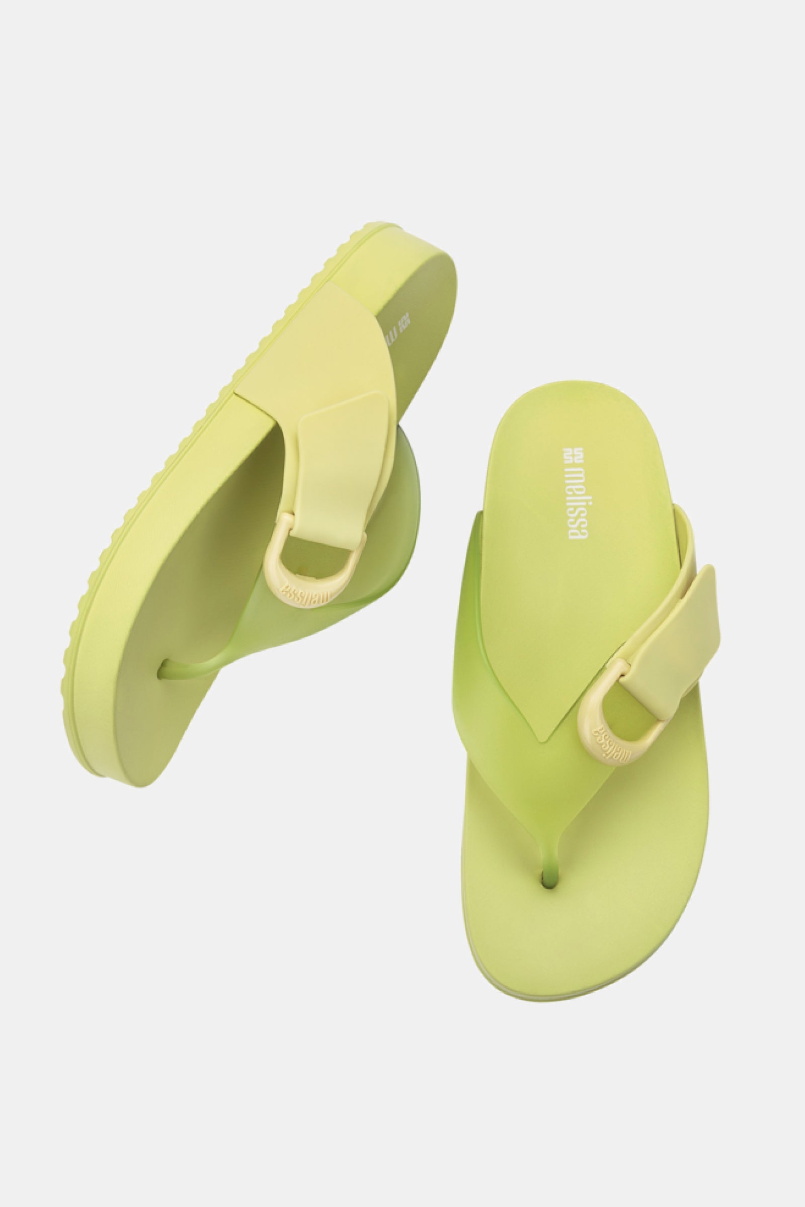 The Melissa Cozy Thong sandals in lime green and yellow feature thick straps and a decorative buckle. Displayed on a white background, one sandal stands upright while the other rests on its side.