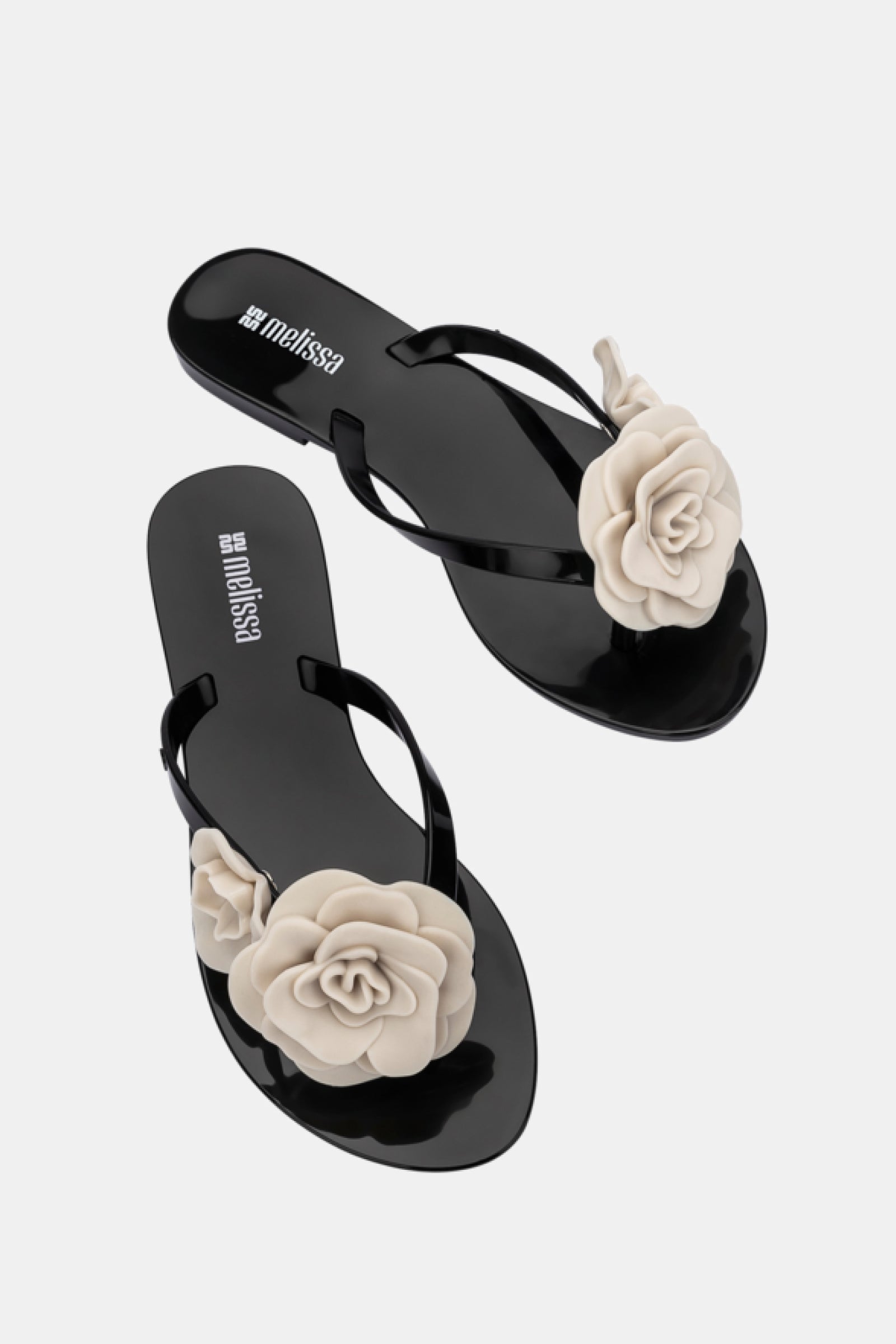 The Melissa Harmonic Petals Sandal is a pair of black flip-flops featuring large beige flower decorations on the straps, shown against a white background.