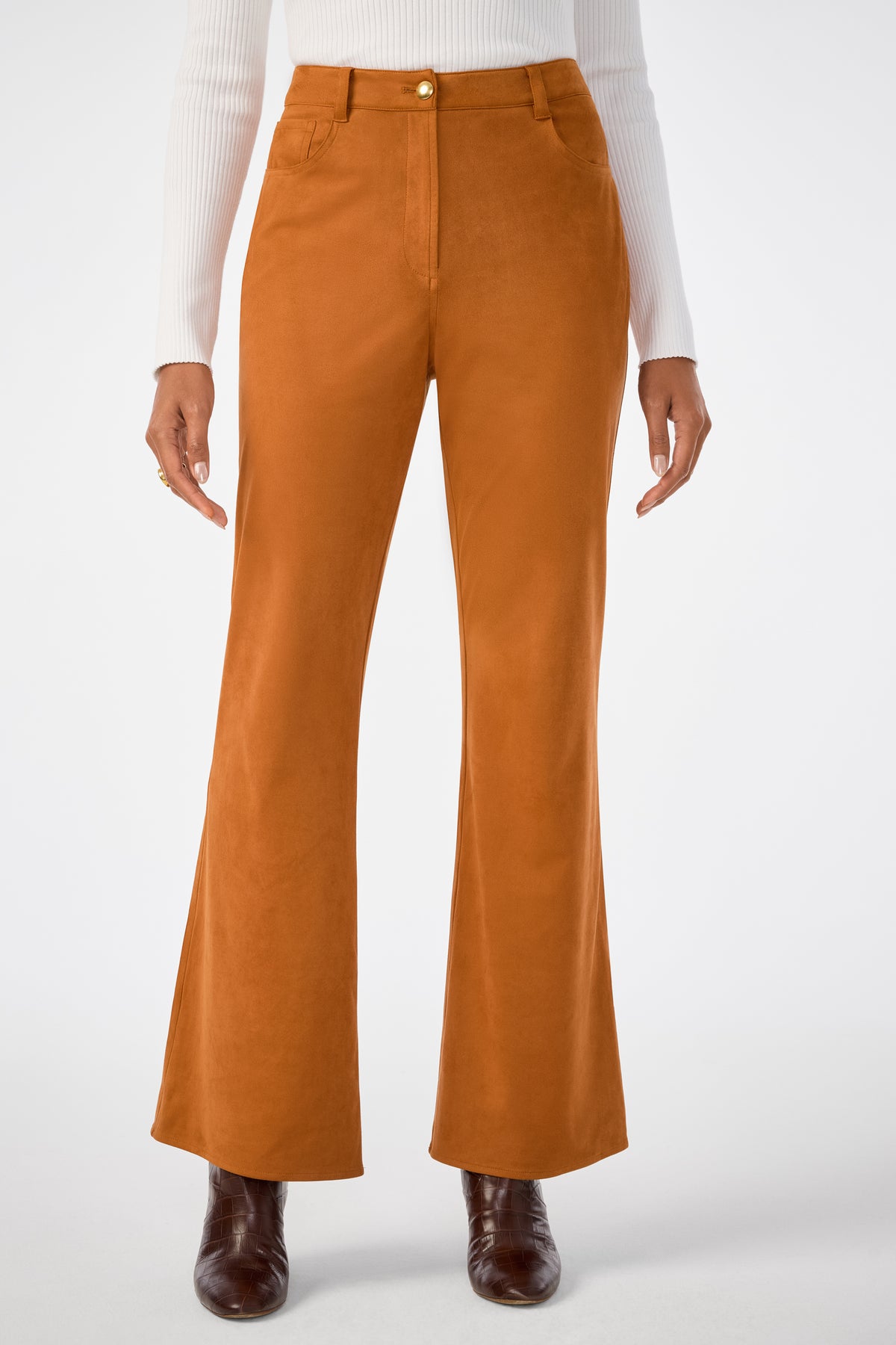 A person wearing the Apple Bottom Pant, high-waisted and rust-colored with a flared cut, paired with a white ribbed long-sleeve top and brown ankle boots, stands against a plain white background.