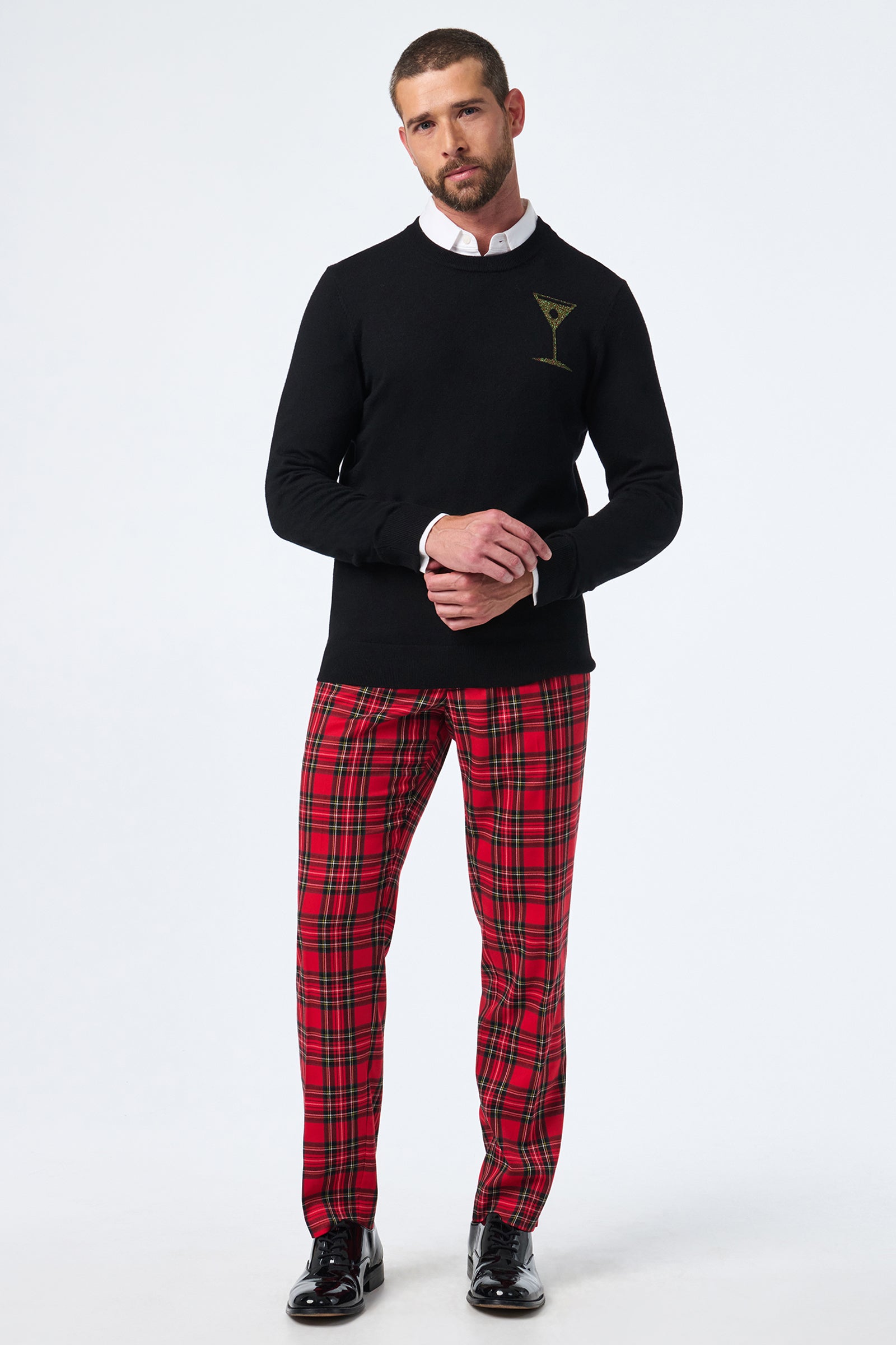 A man stands against a white background wearing the Martini Crewneck, red plaid pants, a white collared shirt, and black dress shoes. His hands are loosely clasped in front of him.