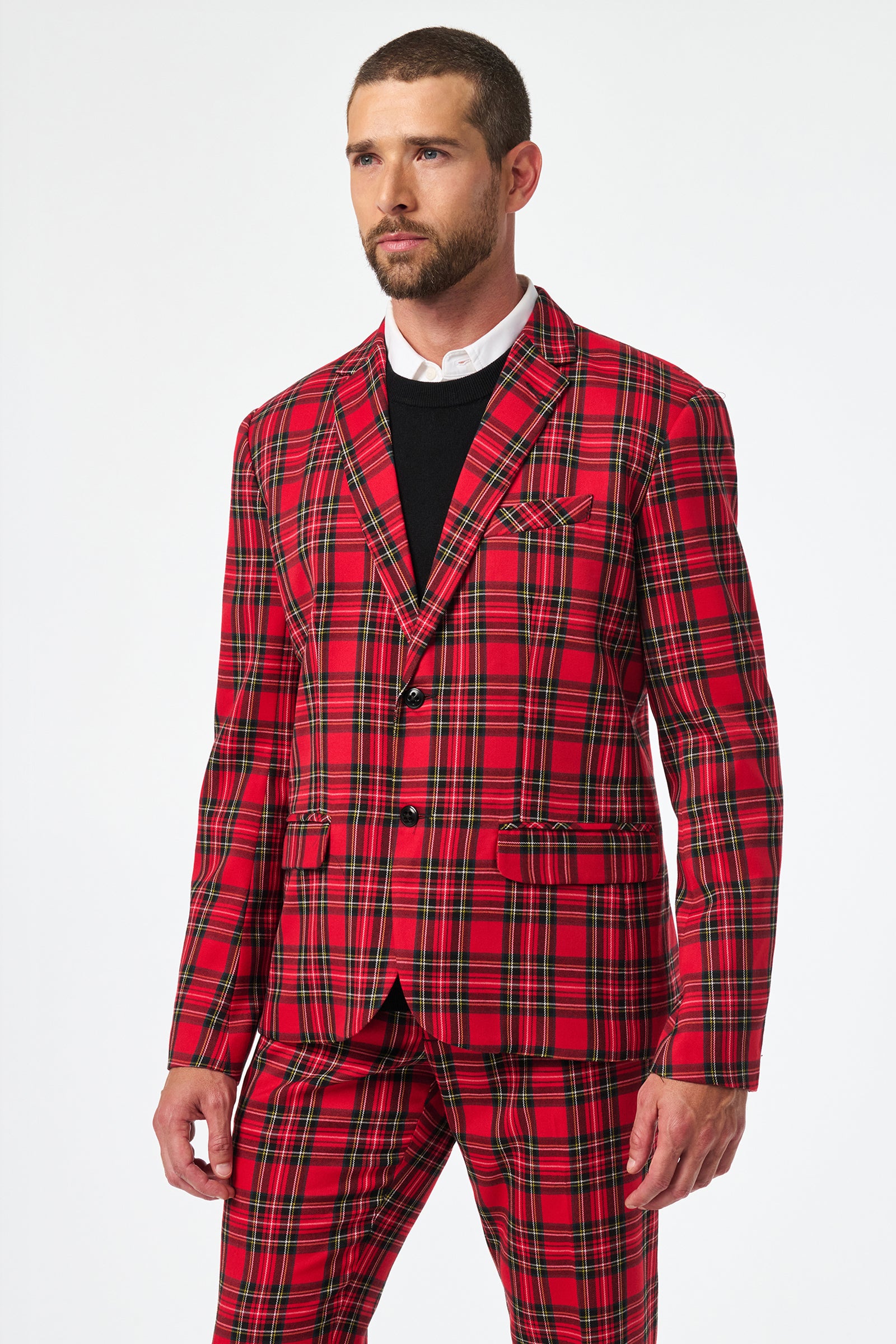 A man in the Thurston Tartan Blazer, featuring red, green, and black plaid, paired with a black sweater and white shirt, stands against a plain white background, looking slightly to the side.