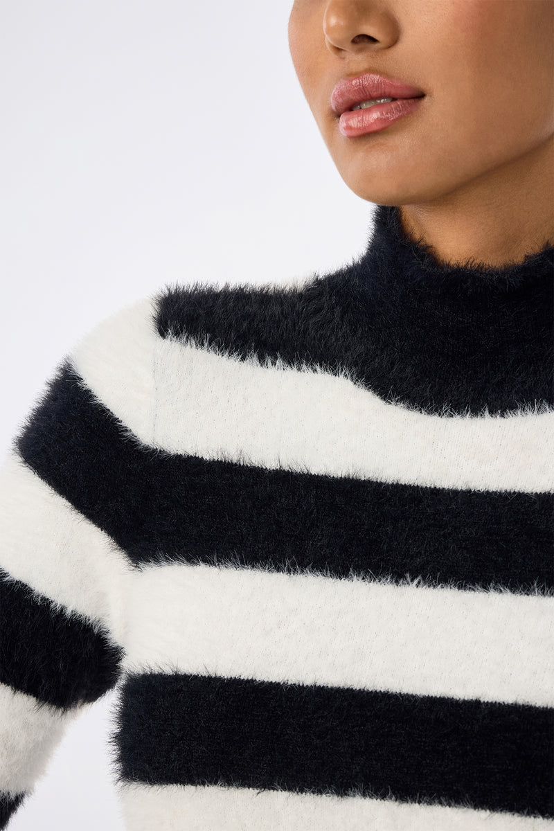 A person wears the Mali Mock Neck Sweater in fuzzy black and white stripes, shown from the shoulders up. Their face is partially visible with lips slightly parted.