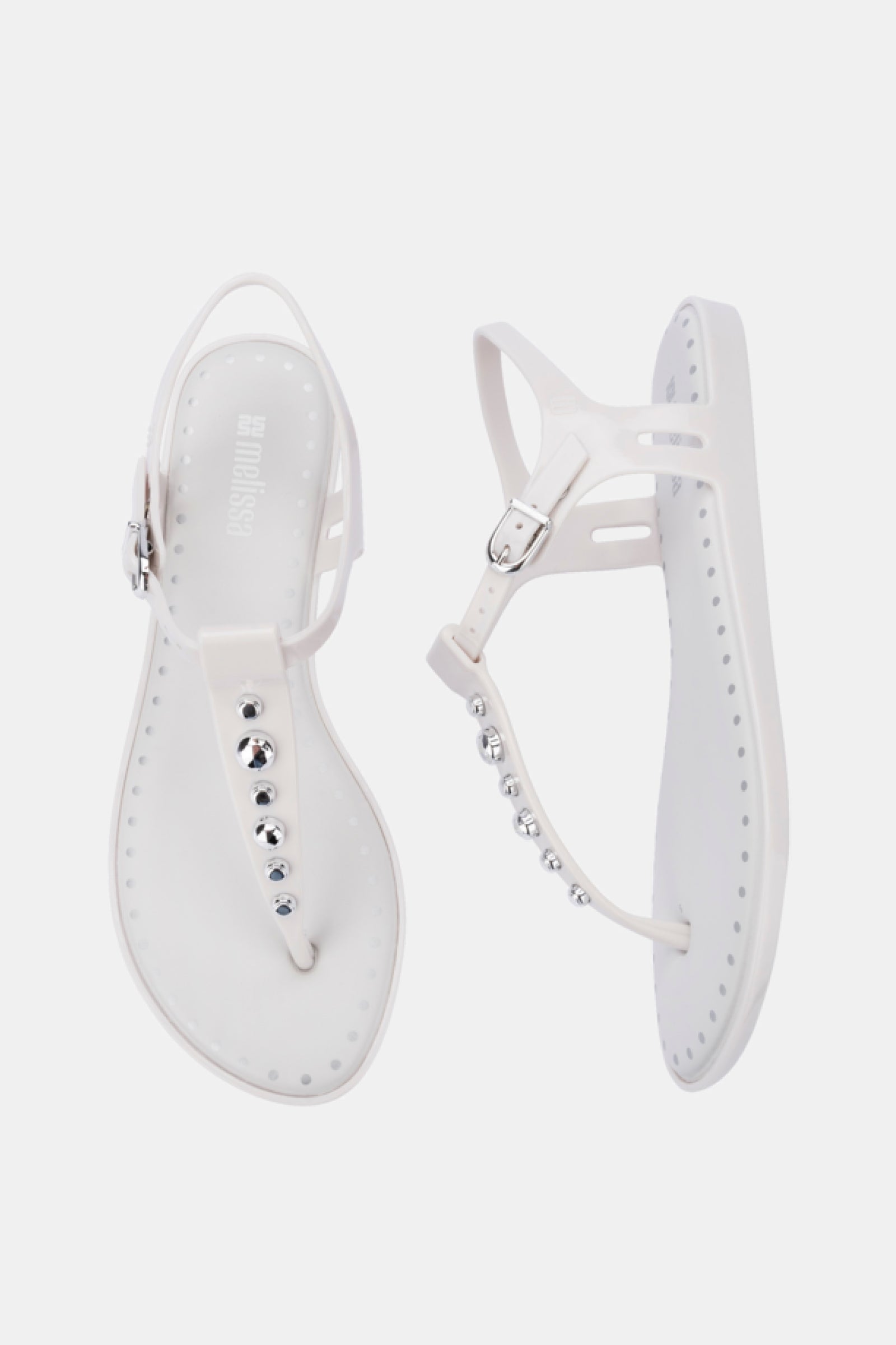 Melissa Solar Boho white flat sandals feature ankle straps and silver stud embellishments on the front strap, shown against a white background.