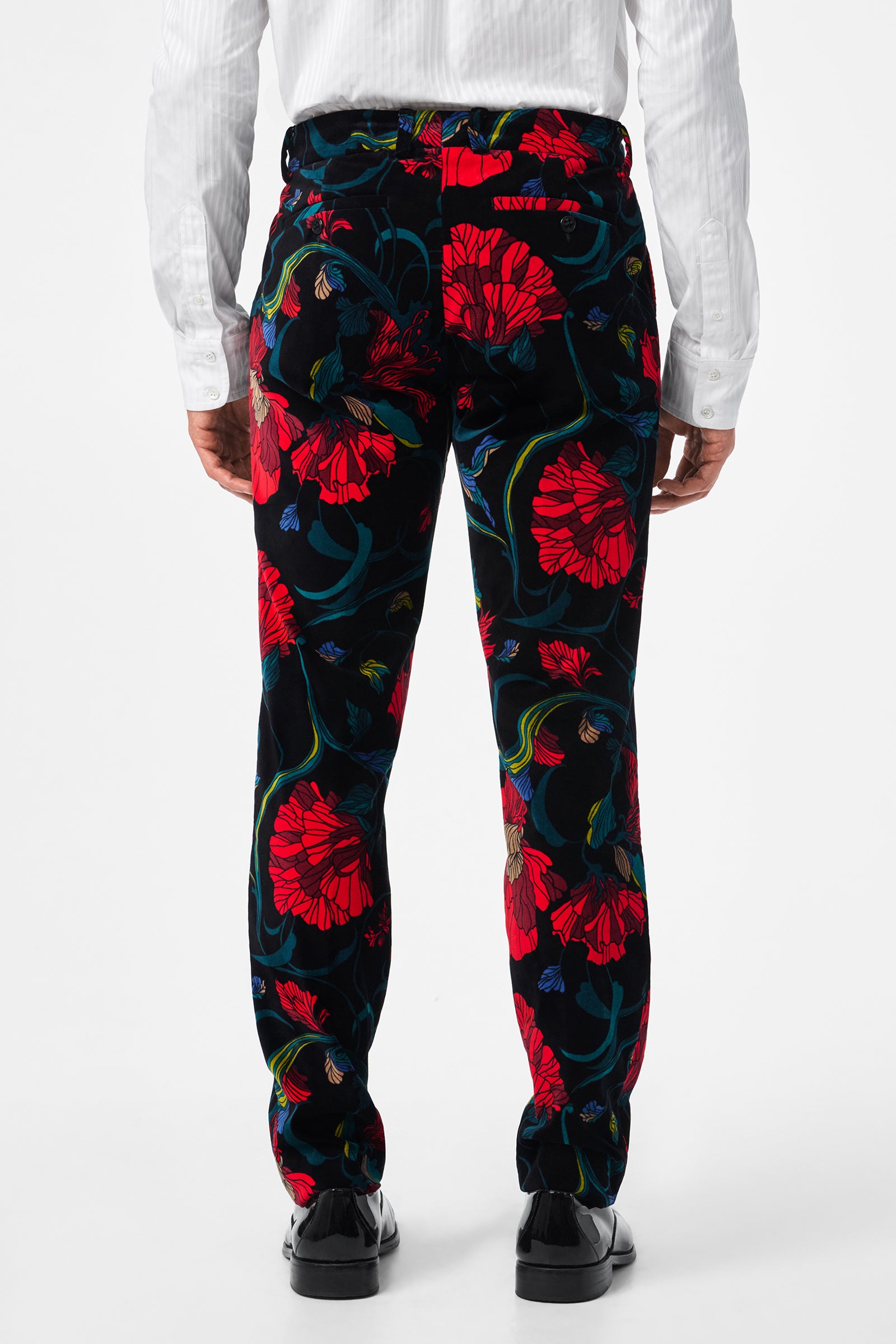 A person is shown from the back against a white background, wearing the Clyde Slim Printed Velvet Trouser featuring a bold red and blue floral print, paired with a white dress shirt and black shoes.