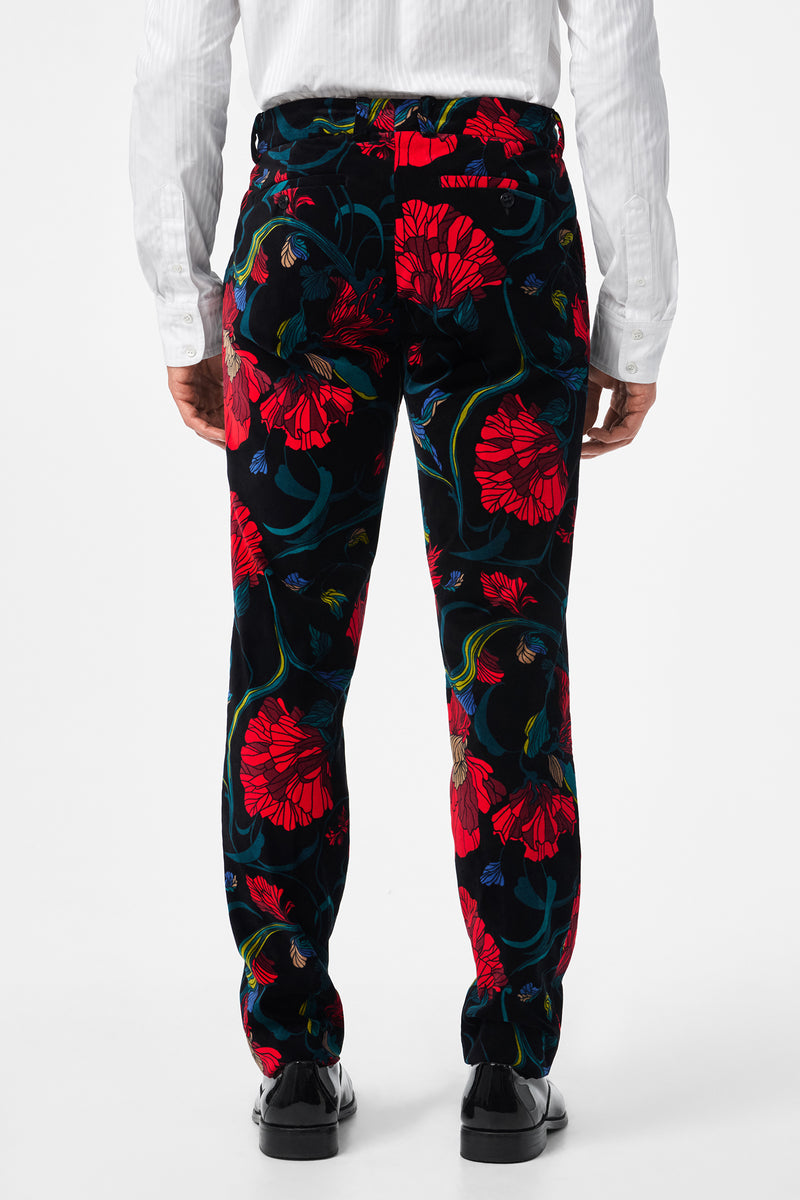 A person is shown from the back against a white background, wearing the Clyde Slim Printed Velvet Trouser featuring a bold red and blue floral print, paired with a white dress shirt and black shoes.