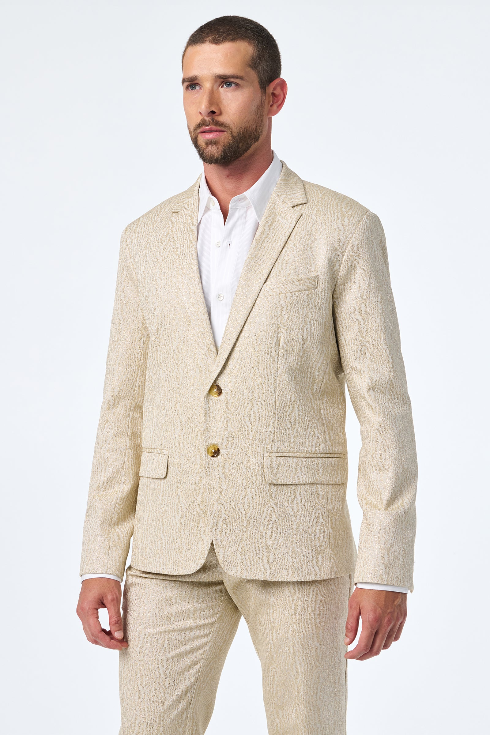 A man with short hair and a beard wears the Thurston Blazer, a light beige patterned suit jacket over a white dress shirt, standing against a plain white background.
