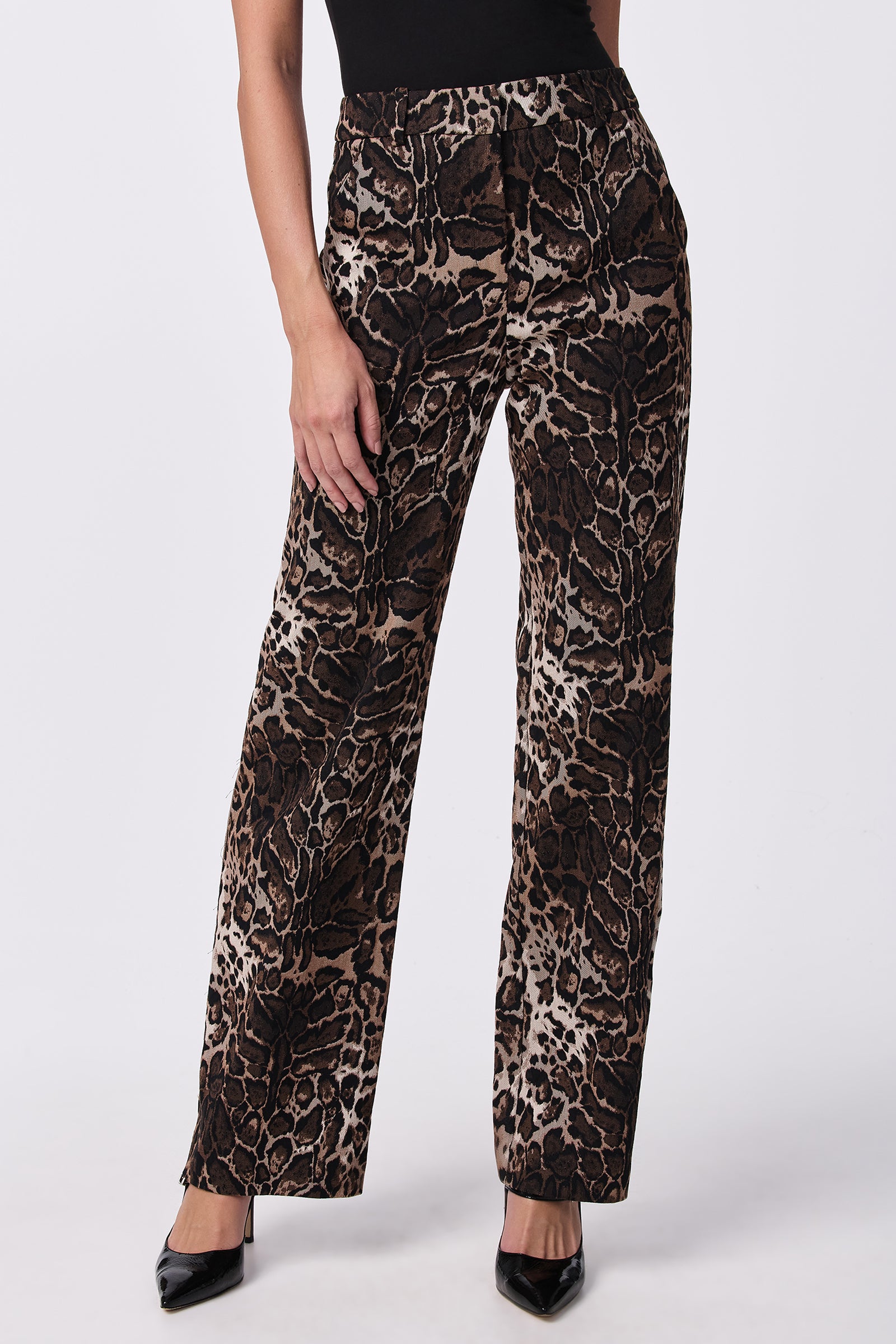 A person wearing Kendi Wed-Leg Pants featuring a brown and black animal print, styled with black pointed-toe heels and a black top. The photo is cropped at the shoulders.