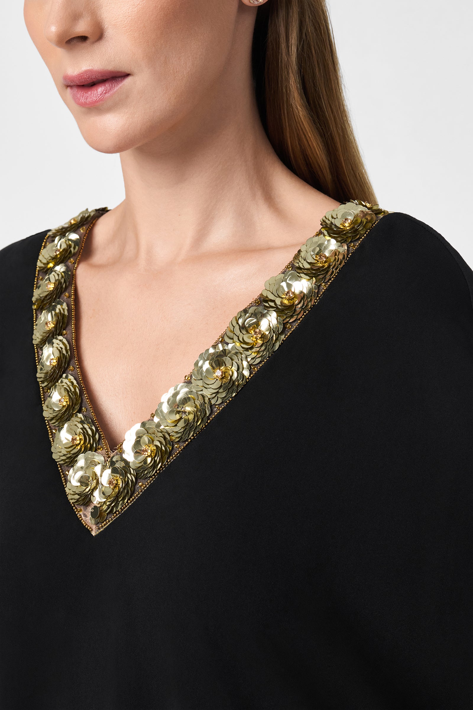 A woman models the Masquerade 3 Dress, a black V-neck outfit featuring ornate gold and white floral trim at the neckline. Only her lower face, neck, and shoulders appear against a plain light background.